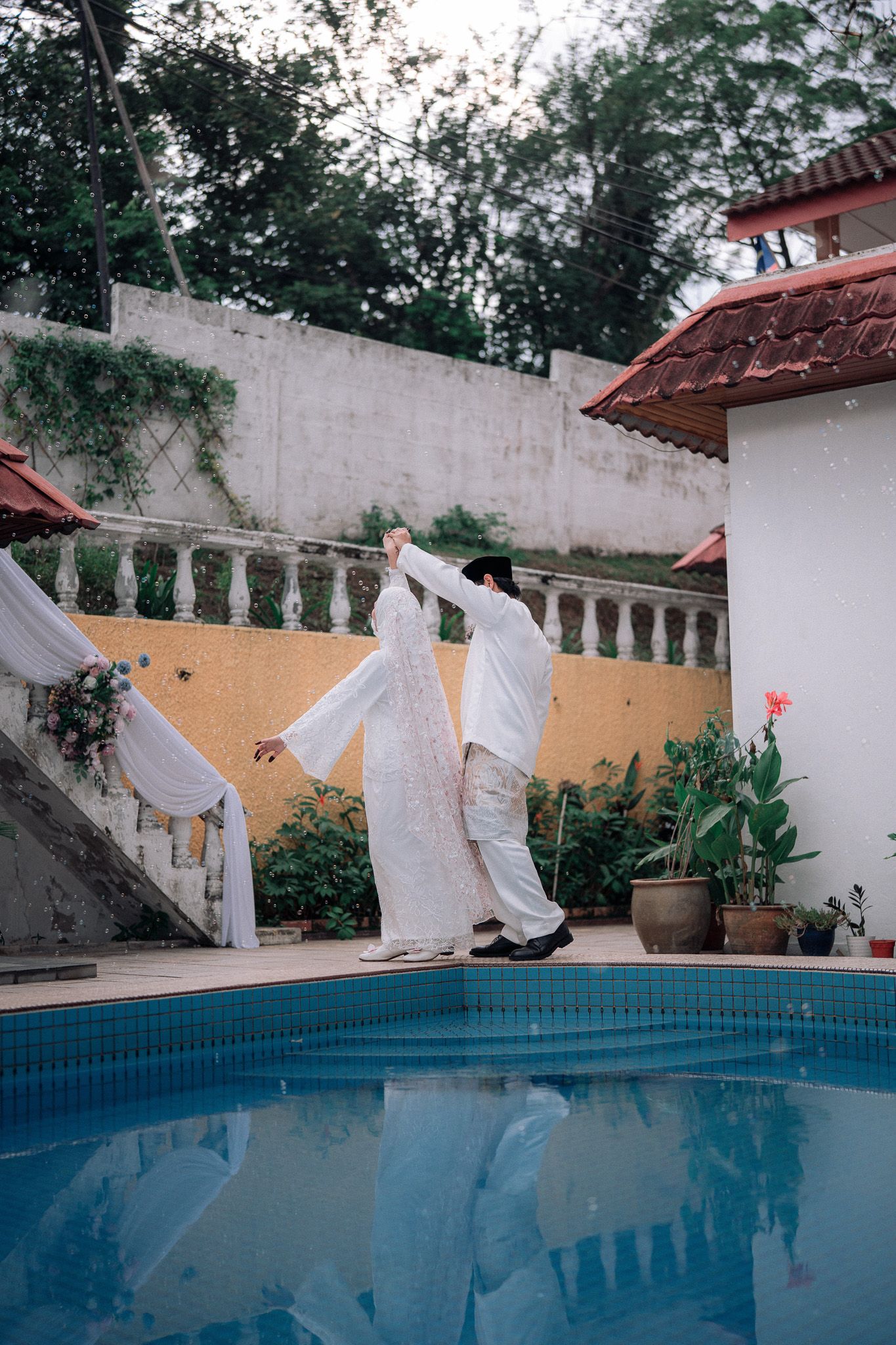 Couple in white attire dancing gracefully by a pool in a tropical garden setting.
