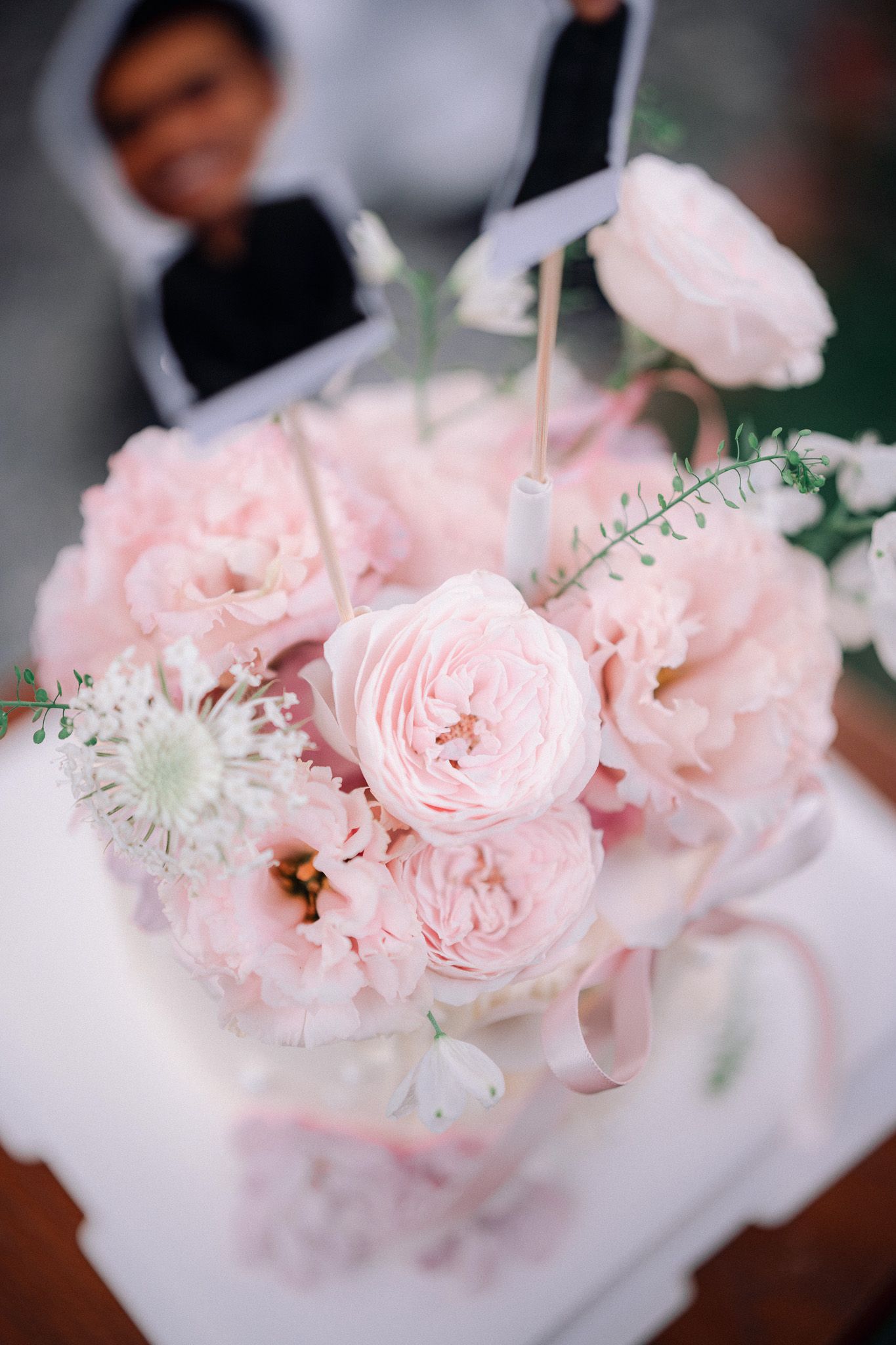 Elegant wedding bouquet of soft pink roses and peonies with white accents on a white table.
