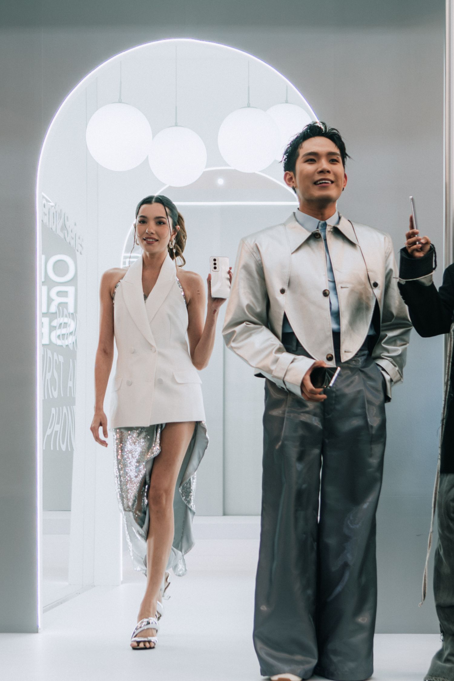 Fashion models pose in modern outfits under an illuminated archway during a presentation.