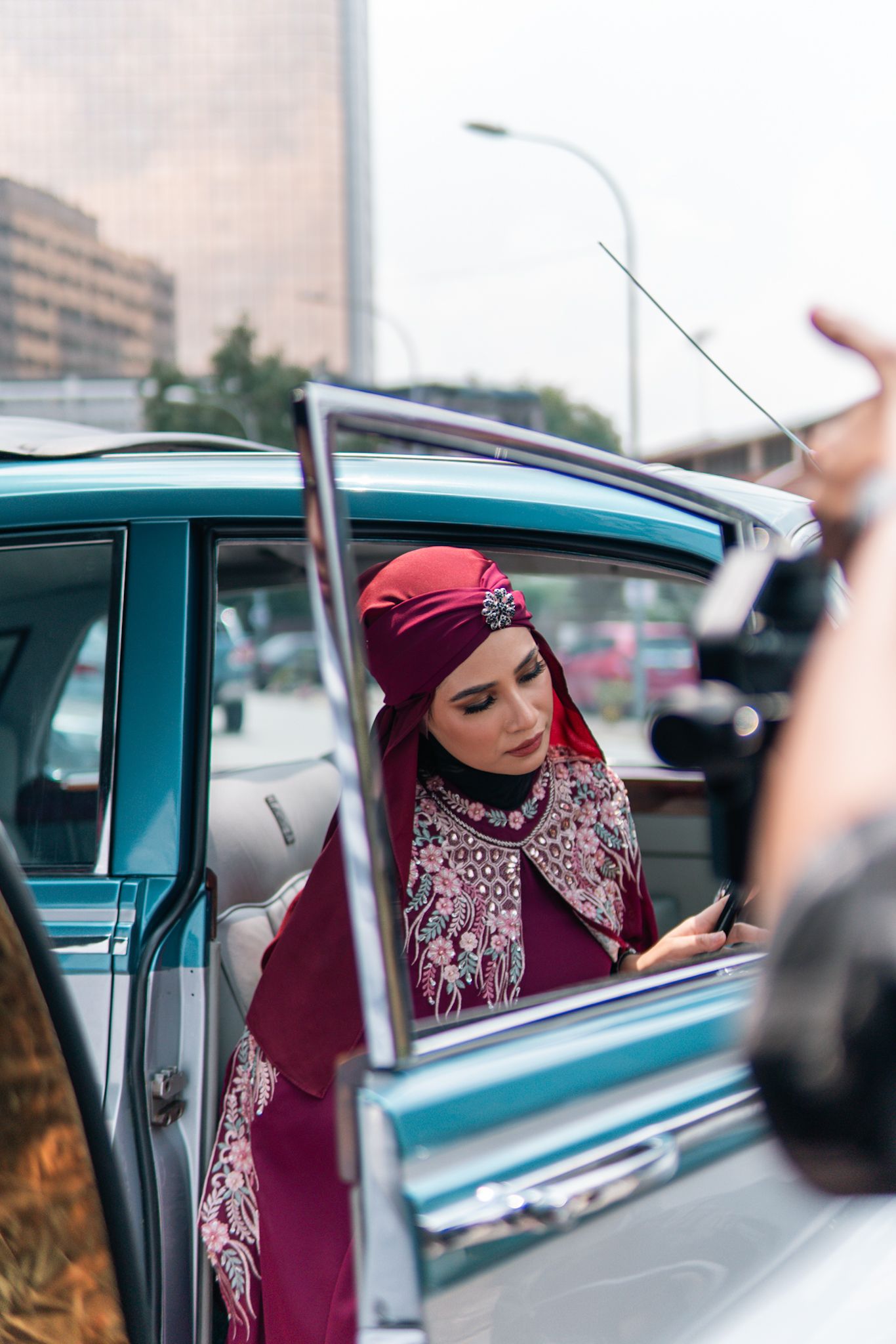 Vintage teal car with open door showcasing elegant burgundy hijab fashion.
