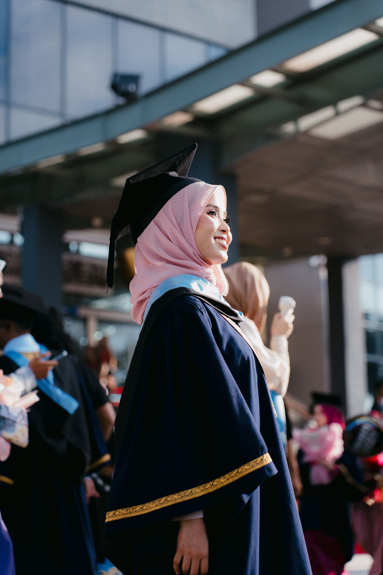 A group of graduates in black robes and hijabs stand together during a graduation ceremony.