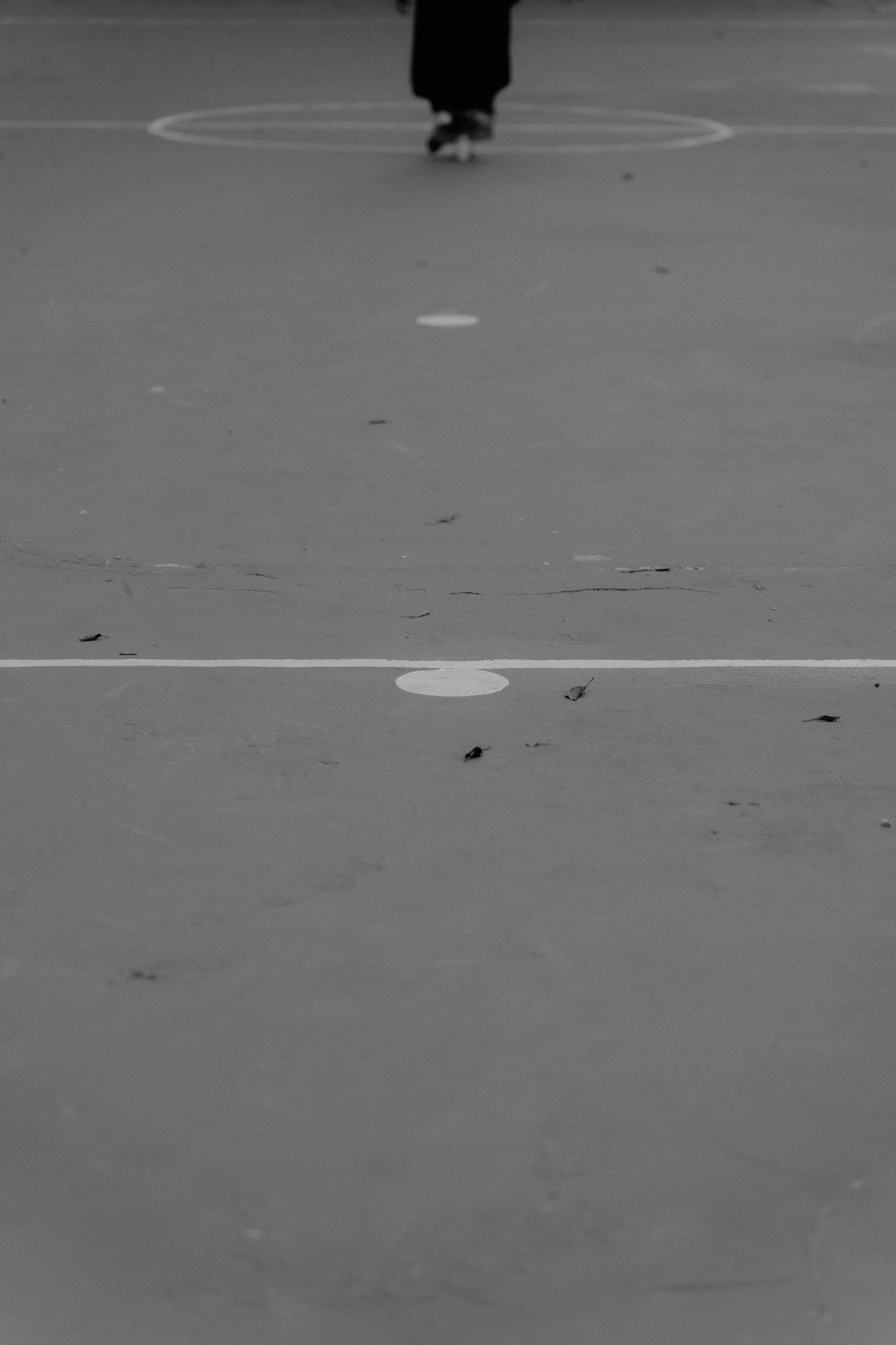 A black and white aerial view shows empty basketball court markings on a concrete surface.