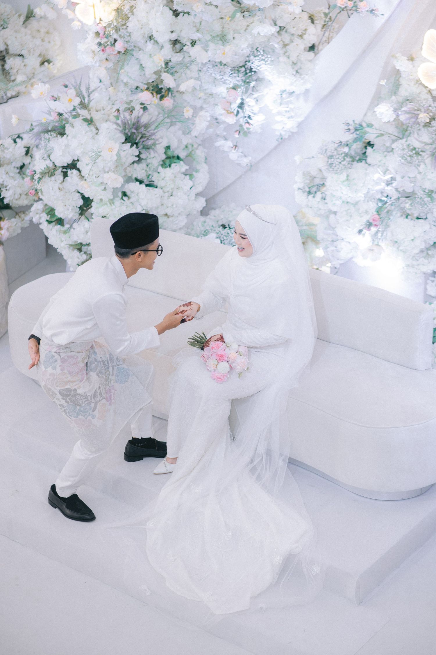 High angle view of a bride in flowing white dress twirling on a white floor surrounded by scattered floral decor.