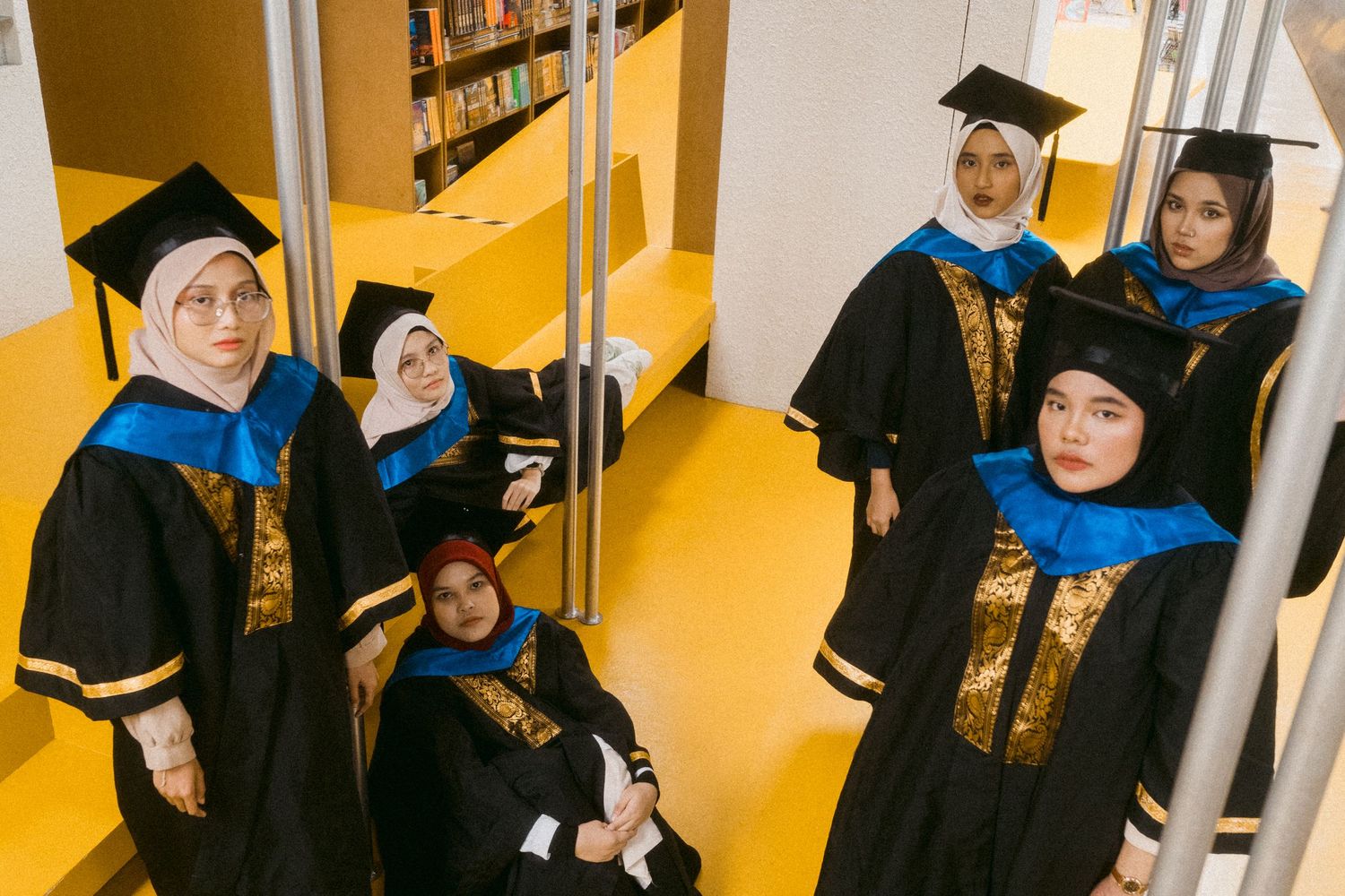 Group photo of graduates in academic regalia in a modern library setting.