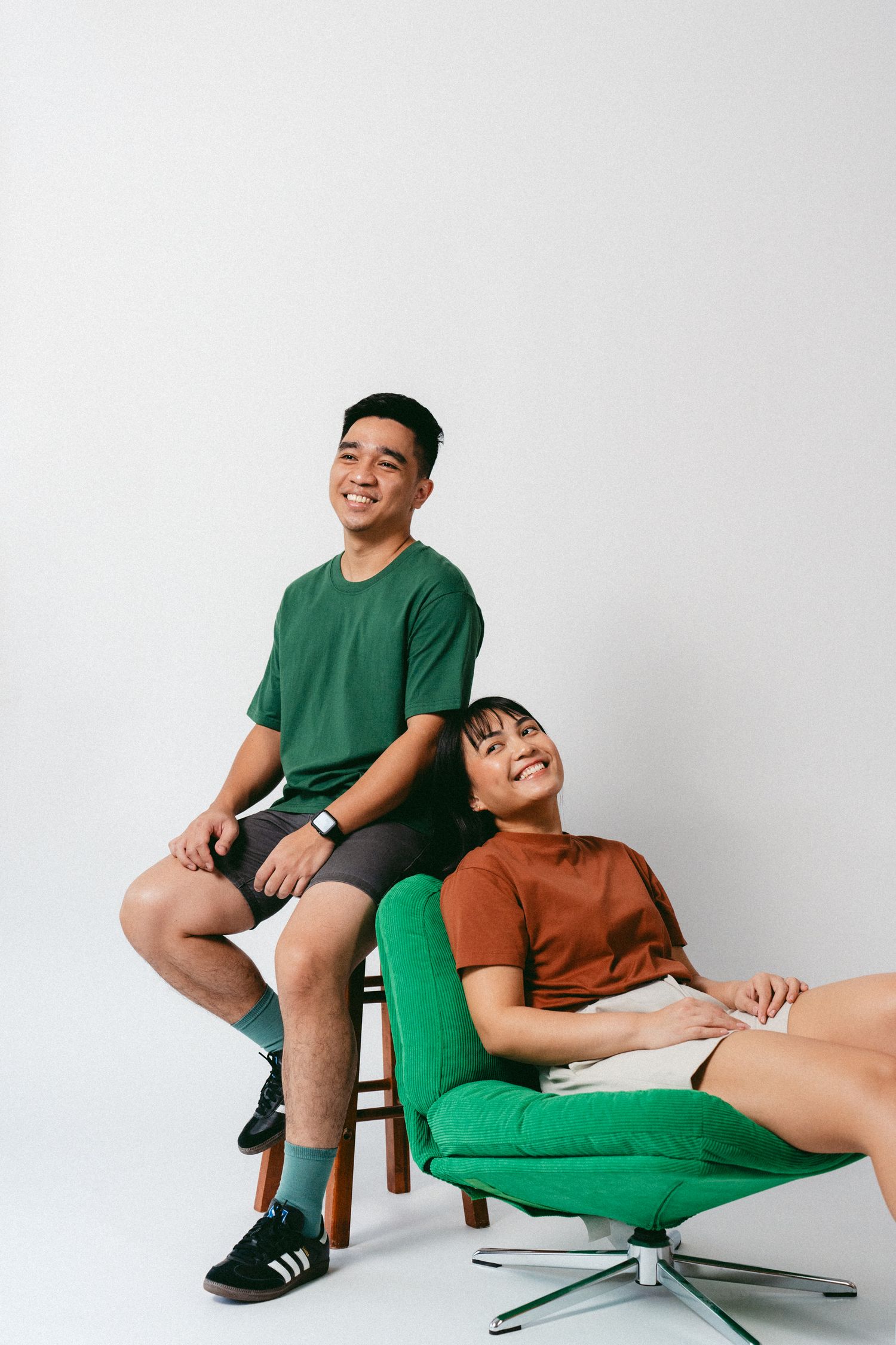 Cheerful couple relaxing on green chair during studio photoshoot.