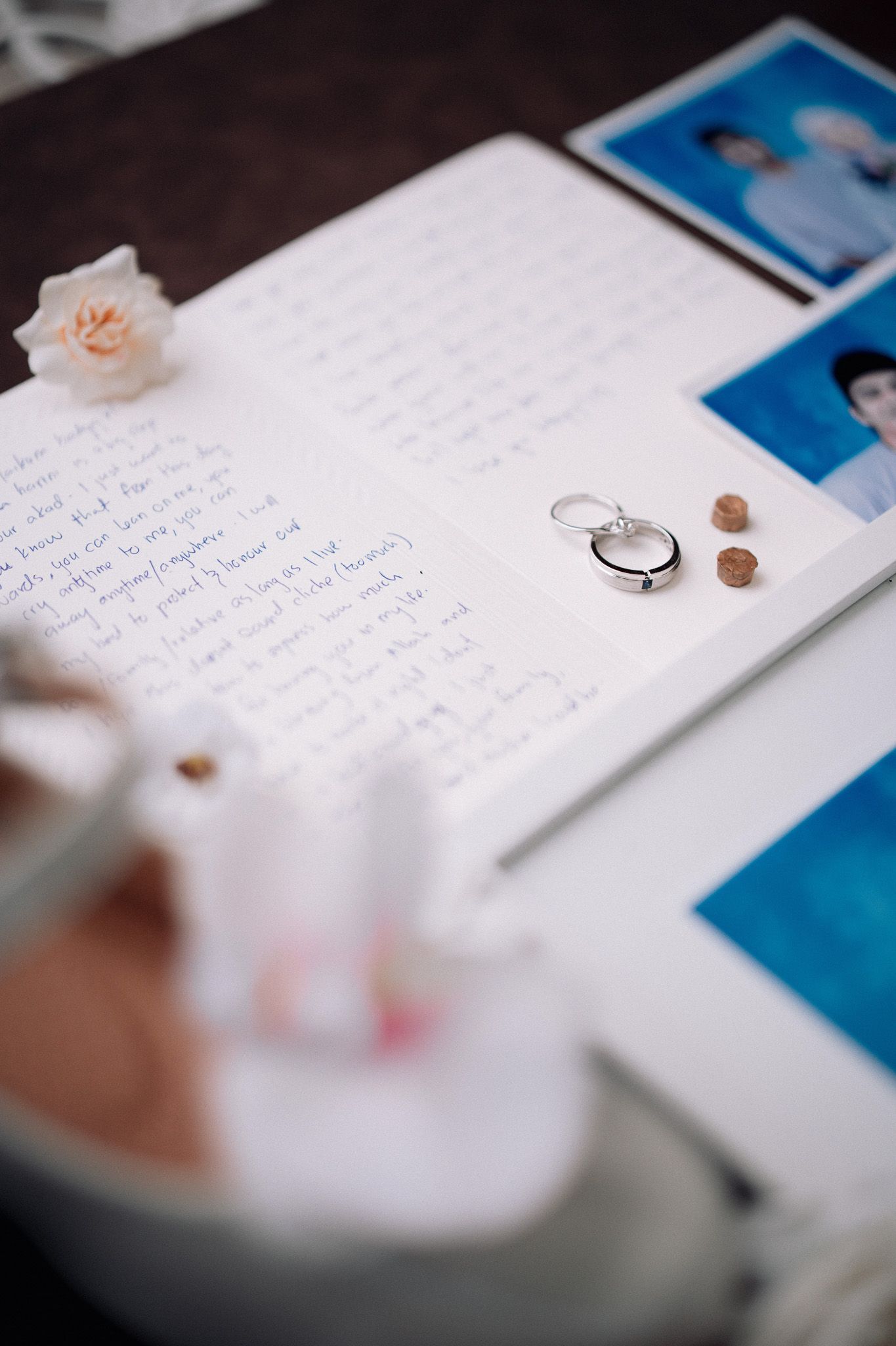 Wedding rings resting on handwritten vows with photos and a delicate pink rose, capturing romantic pre-ceremony details.