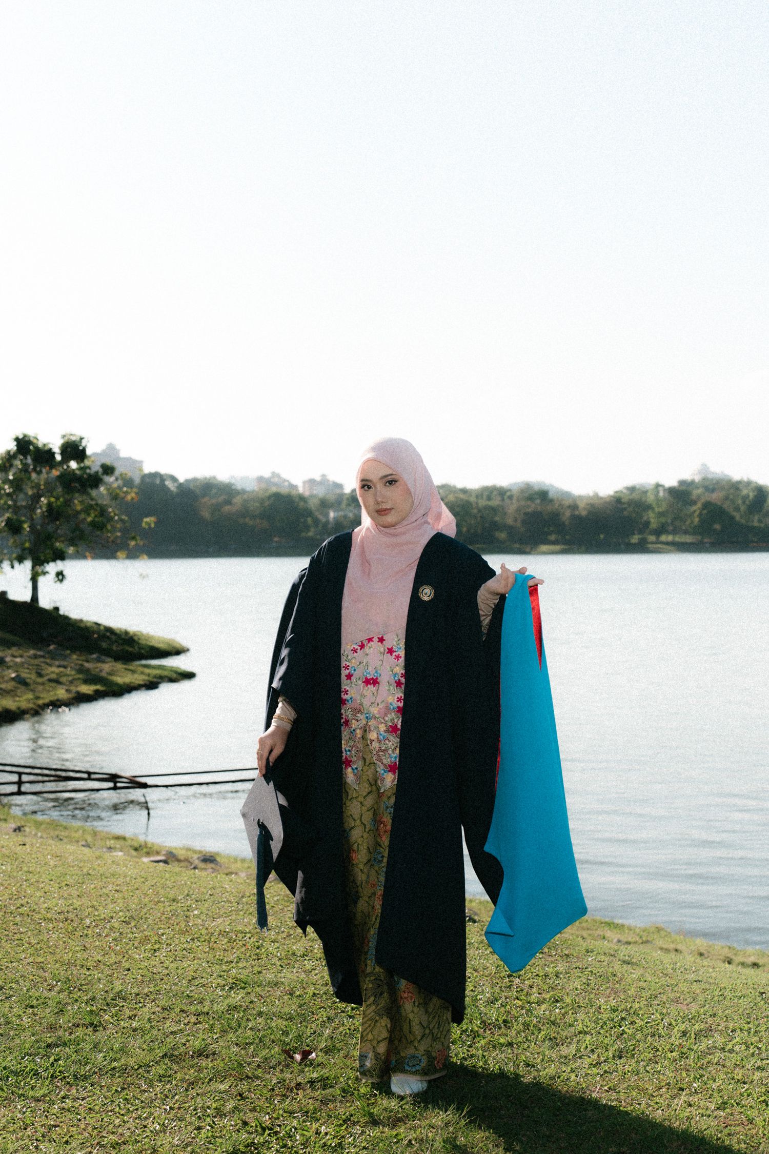 A person in dark clothing stands by a waterfront on grassy terrain during golden hour.
