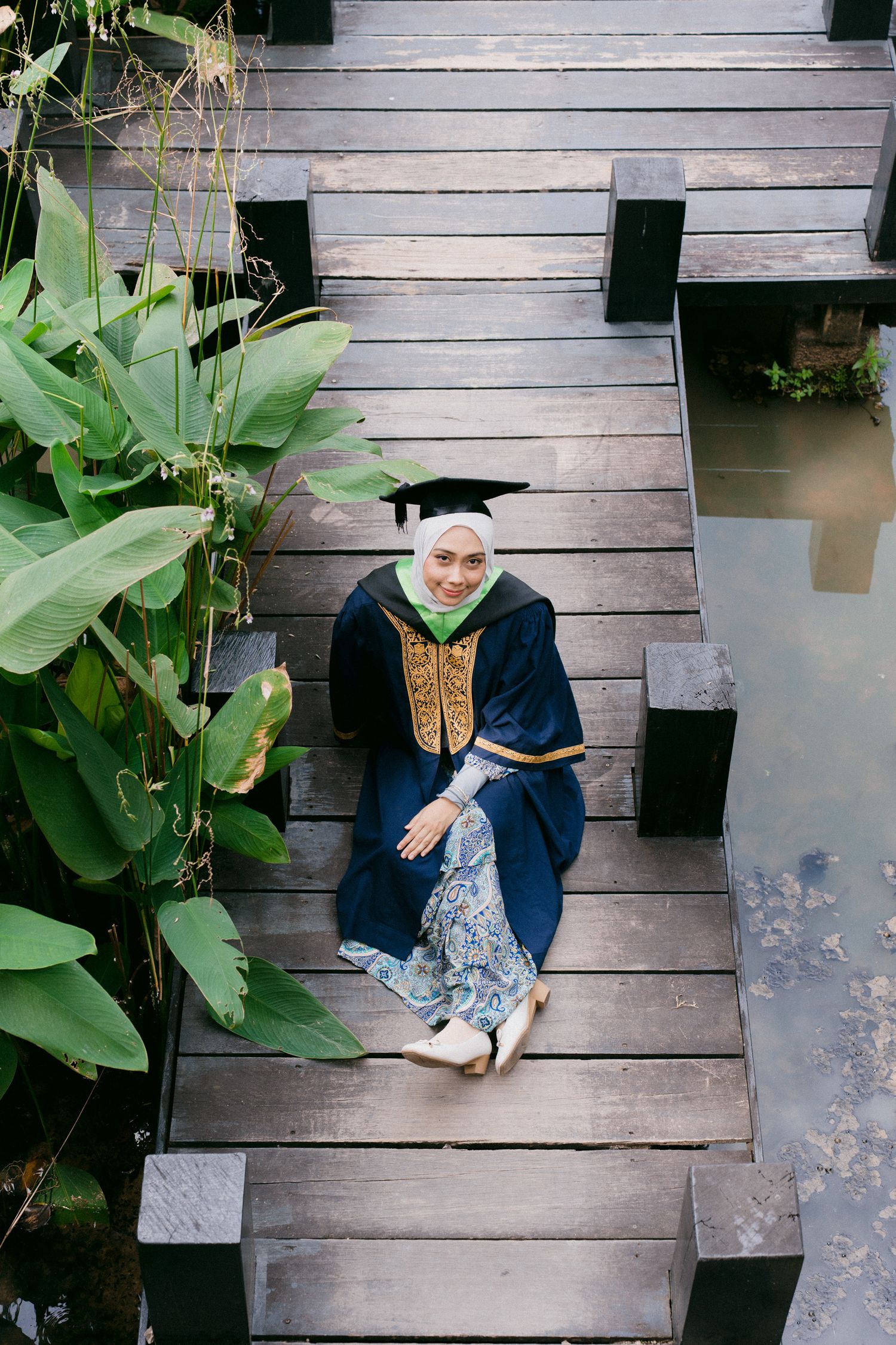 Person in navy blue outfit and leopard print shoes sits on wooden deck surrounded by tropical plants.