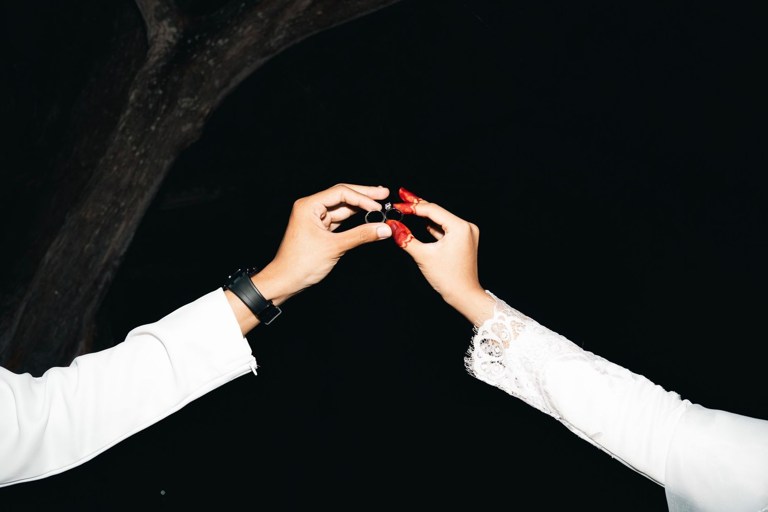 Two hands in white sleeves reaching toward each other against a dark background, one holding a small red object.