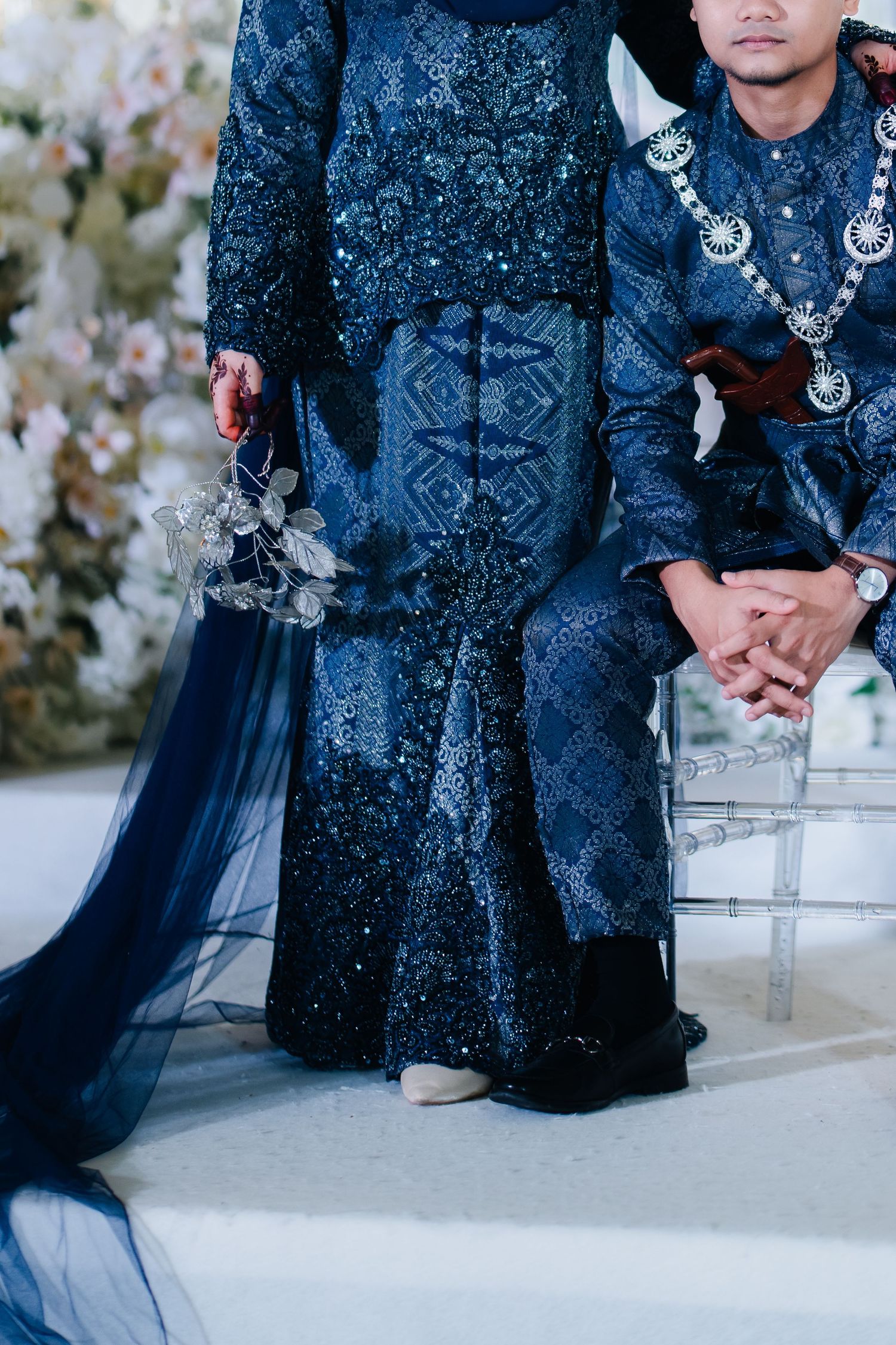 Close-up of traditional blue Malay wedding attire with intricate beading and flowing fabric details.