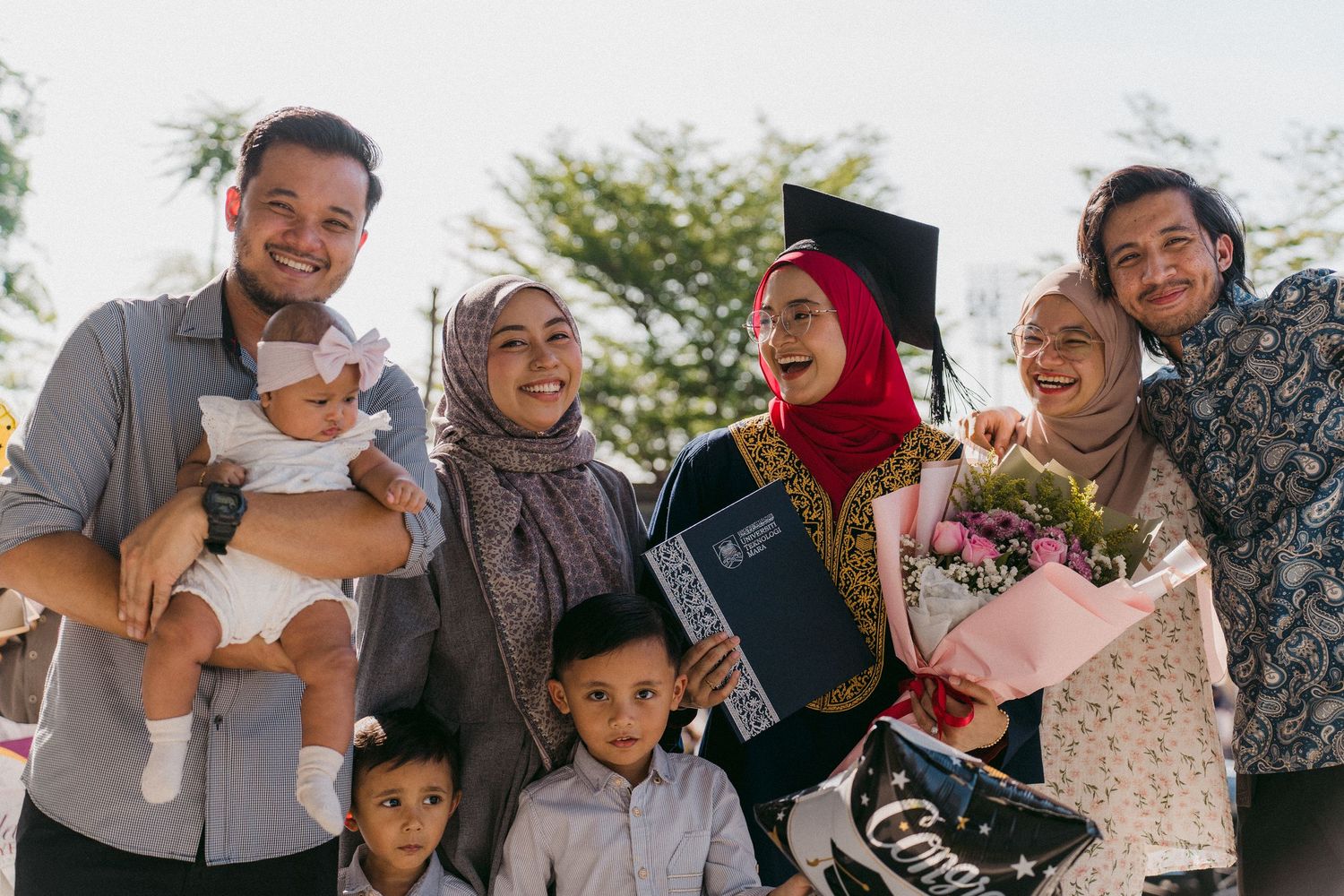 A joyful graduation celebration with family members wearing hijabs and traditional dress gathered together outdoors.
