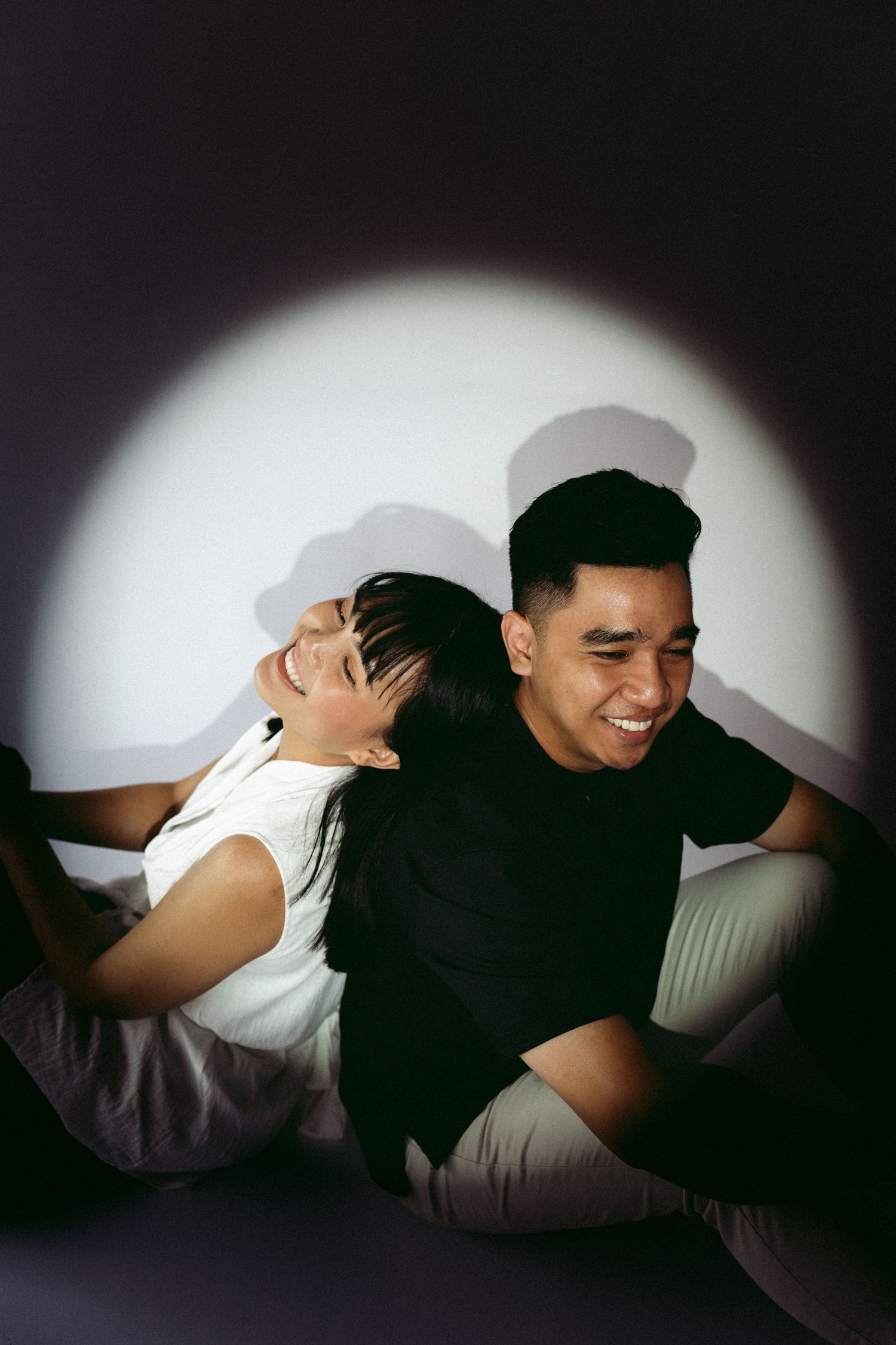 A joyful couple sharing a candid laughing moment in front of a spotlight backdrop.