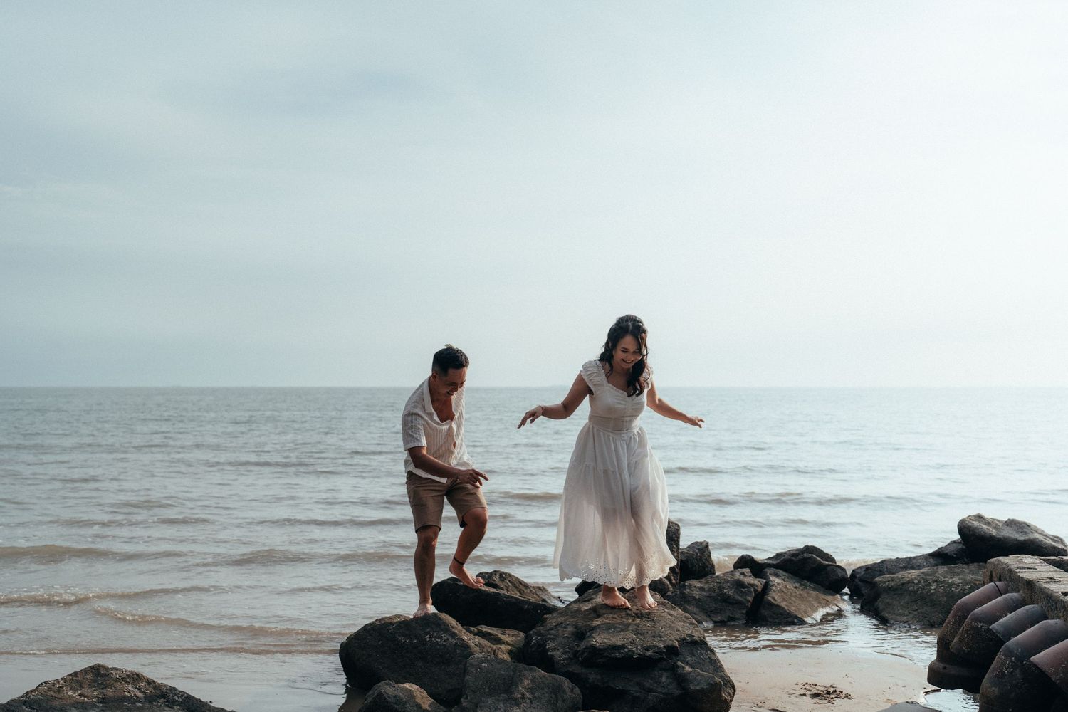 A couple carefully balancing on coastal rocks by the ocean.