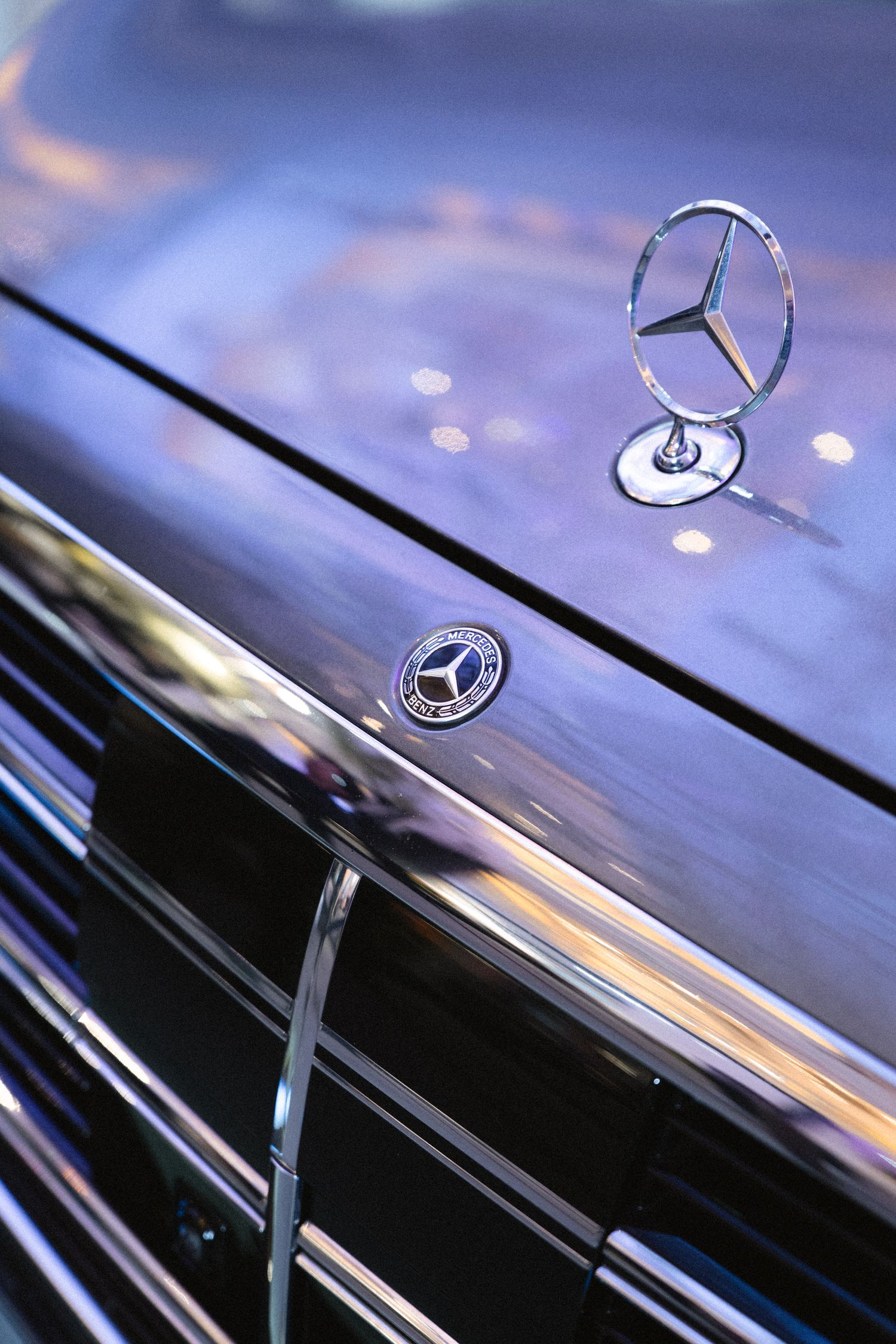 Close-up of a Mercedes-Benz hood ornament and emblem on a blue luxury car.