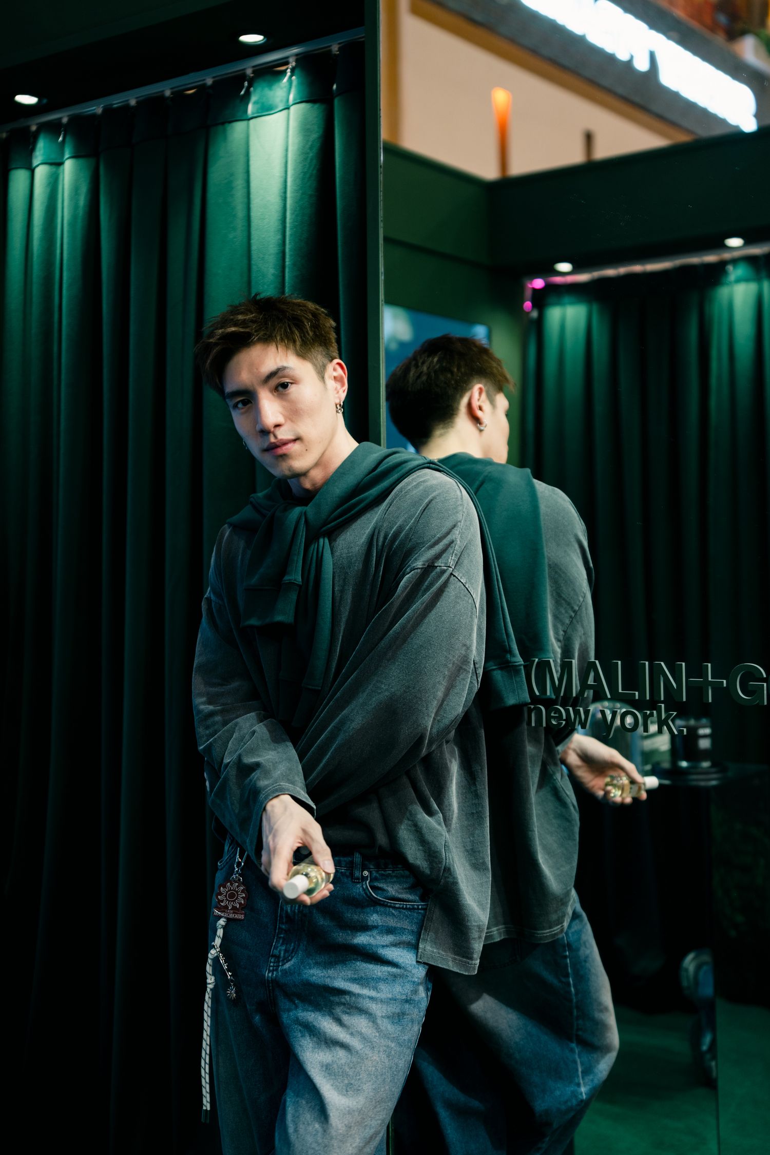A casual scene in front of dark green curtains showing a gray hoodie reflection in a mirror at night.
