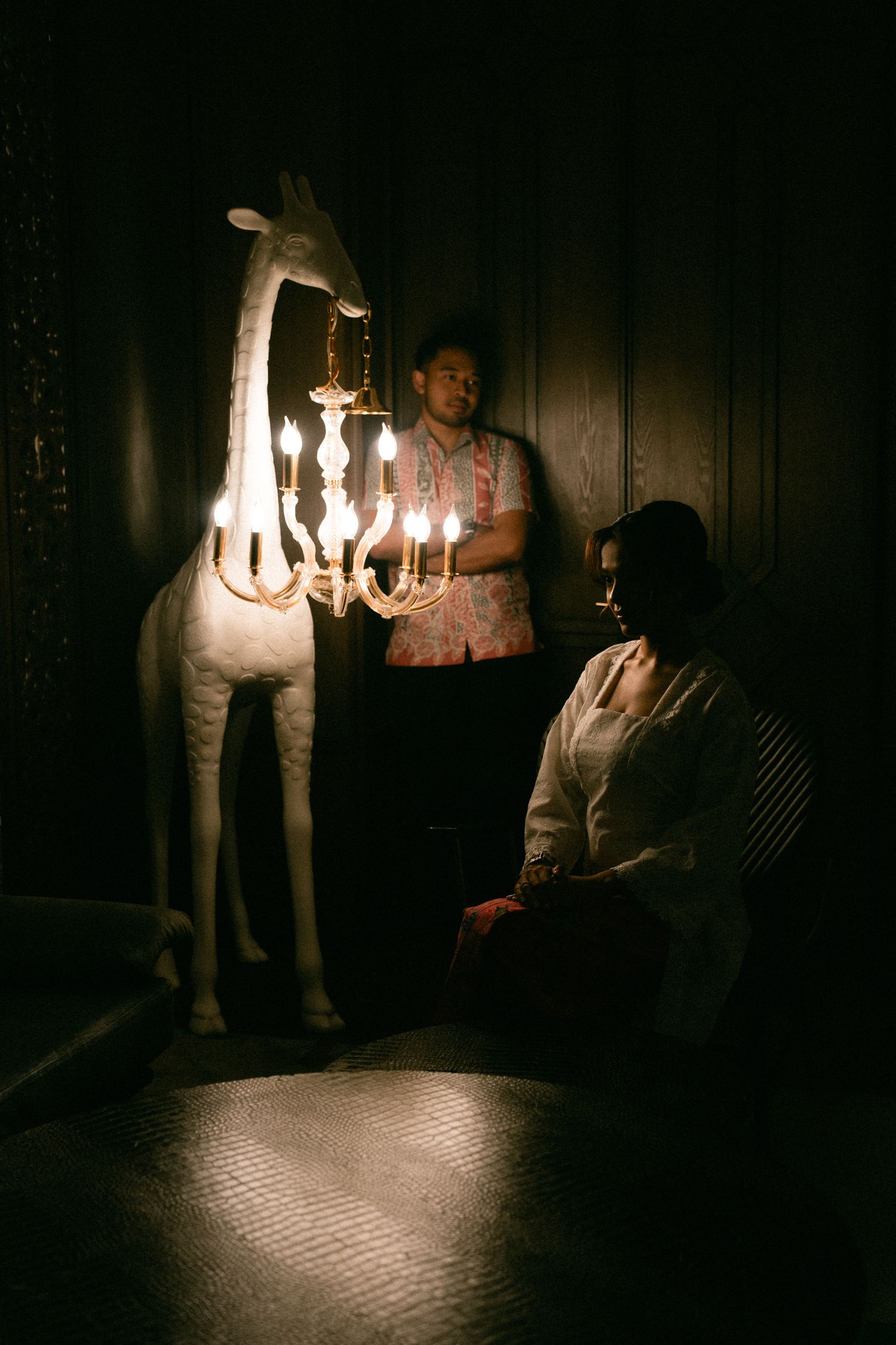 A unique giraffe-shaped lamp with candle lights illuminates a dark room in moody, atmospheric lighting.