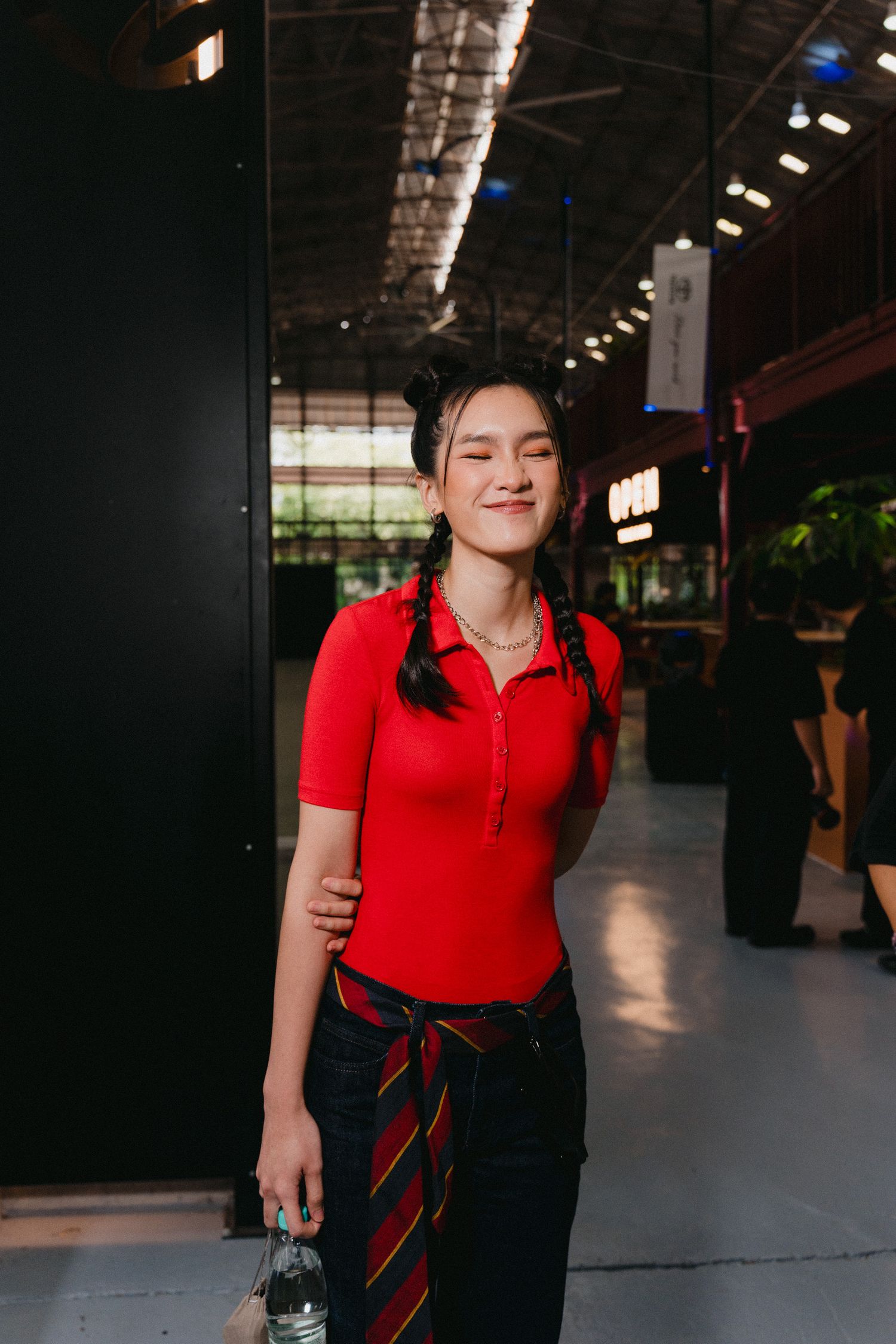A person in a red polo shirt and black skirt stands in a dimly lit industrial space.