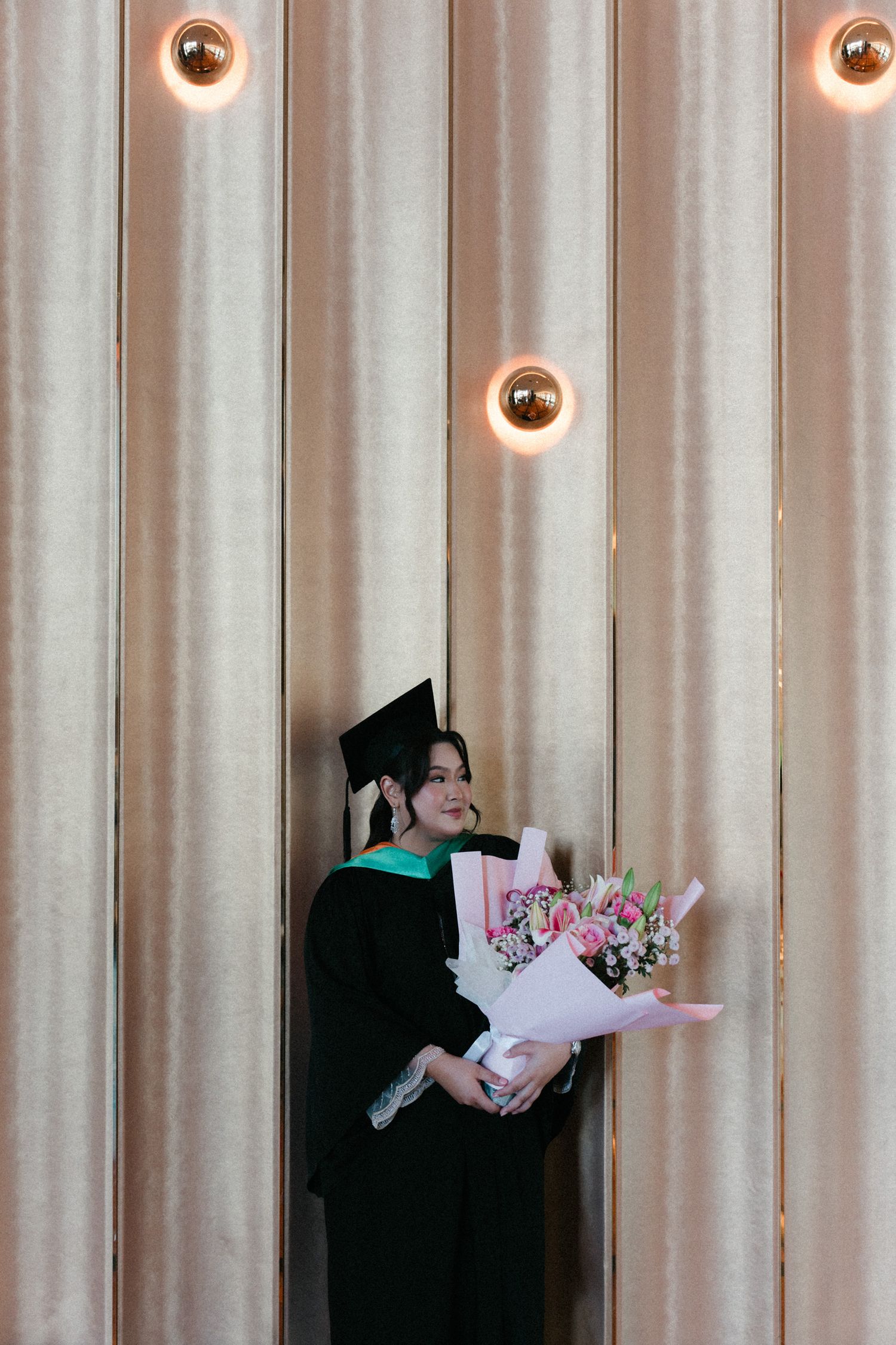Three bouquets of pink flowers displayed against a beige striped wall with circular light fixtures.