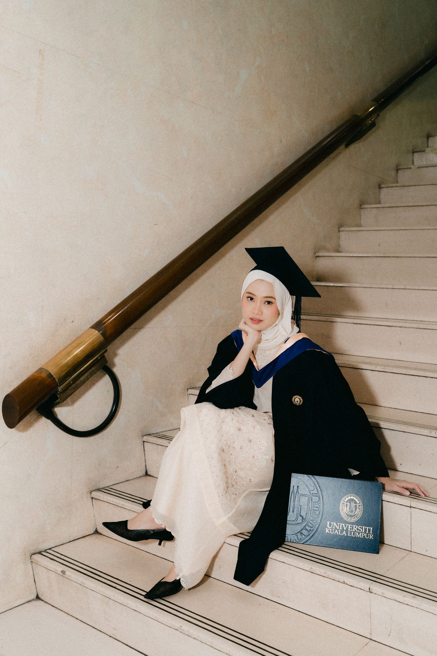 A graduation photo series showing a person in cap and gown sitting on white stairs in different artistic poses.