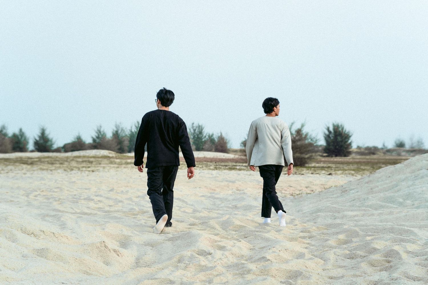 Two figures walking away on a sandy path surrounded by natural landscape.