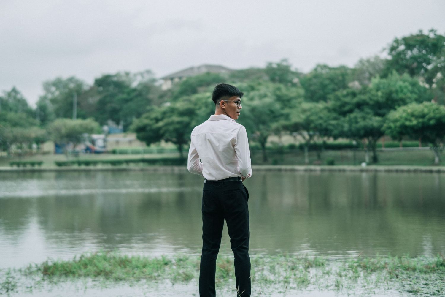 Person in white shirt and black pants standing by lake in contemplative pose.