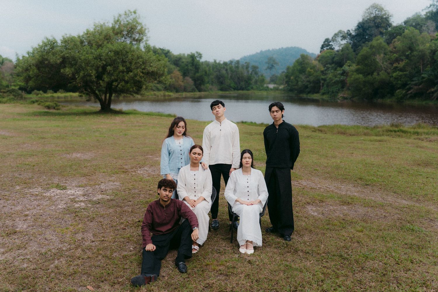 A group of people in casual attire pose together on grass with a serene lake and mountains in the background.