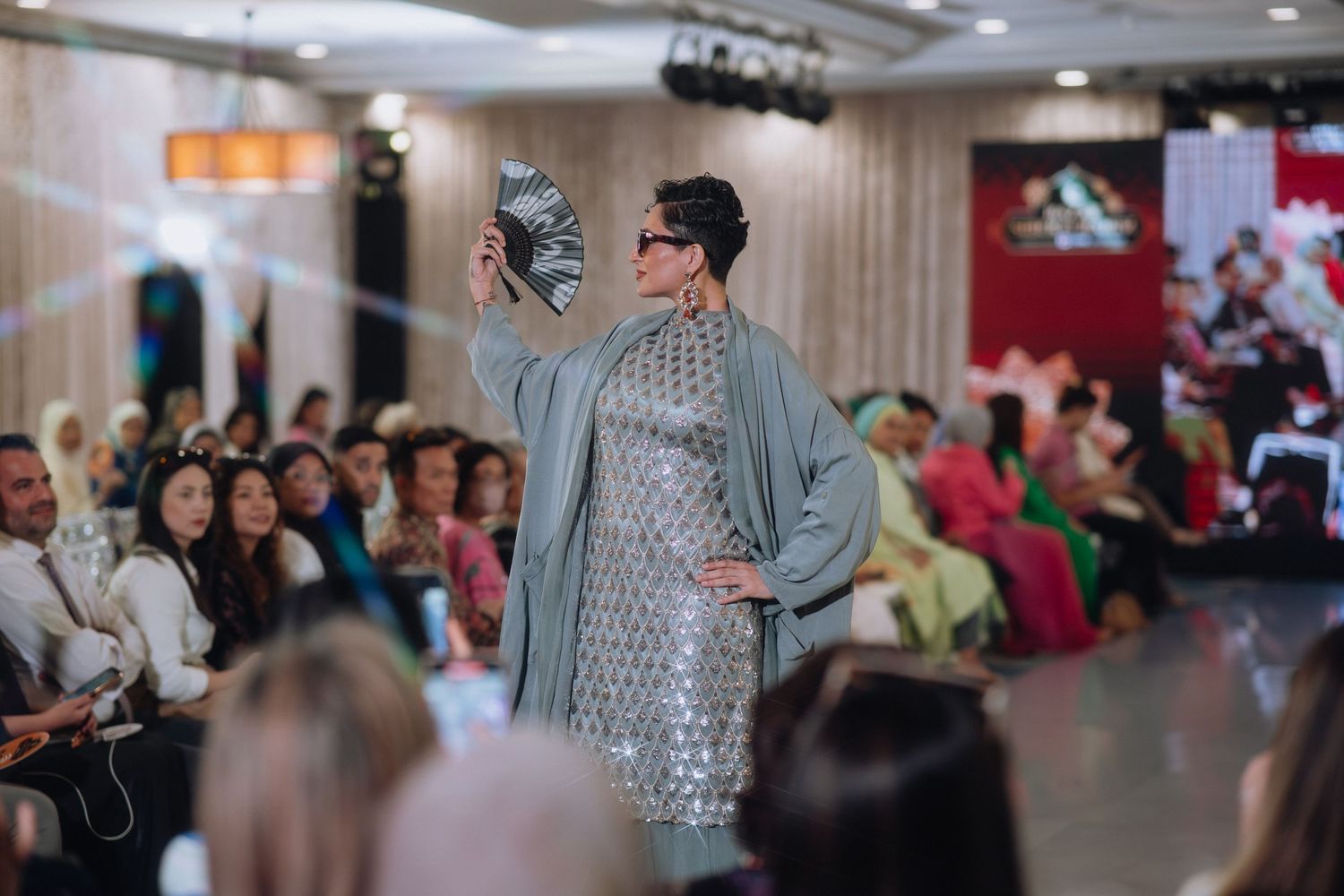 Model showcases metallic gray traditional dress at indoor fashion show.