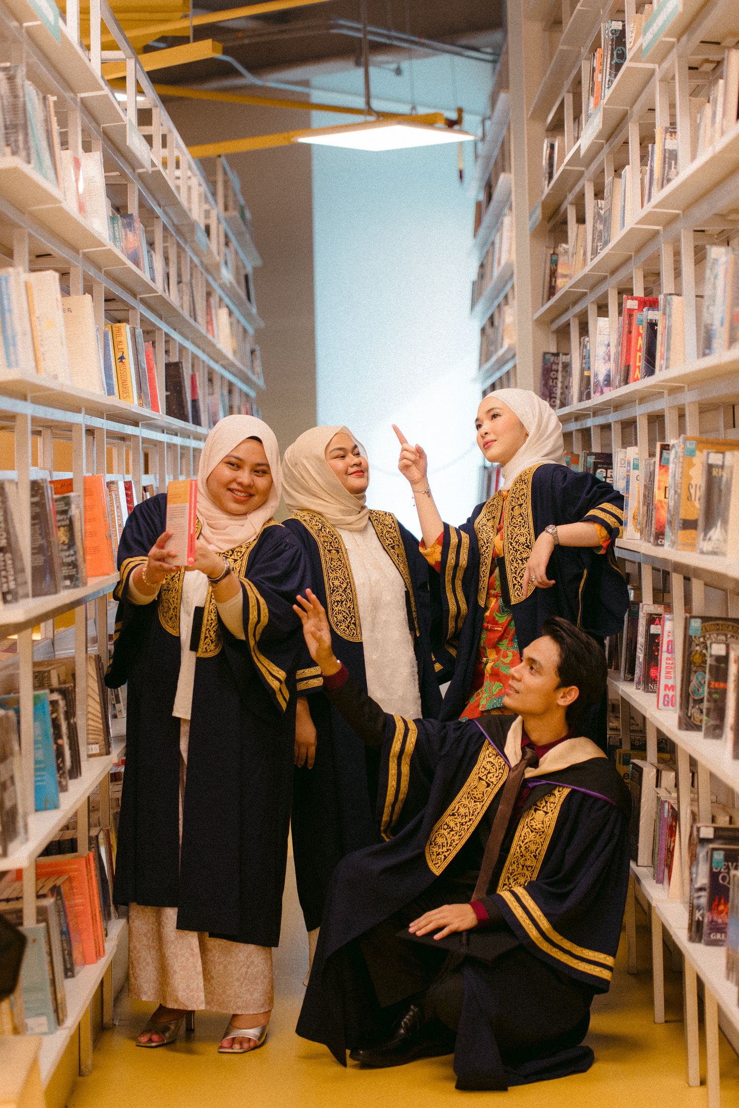 Graduates in black and gold academic regalia celebrate among library bookshelves.