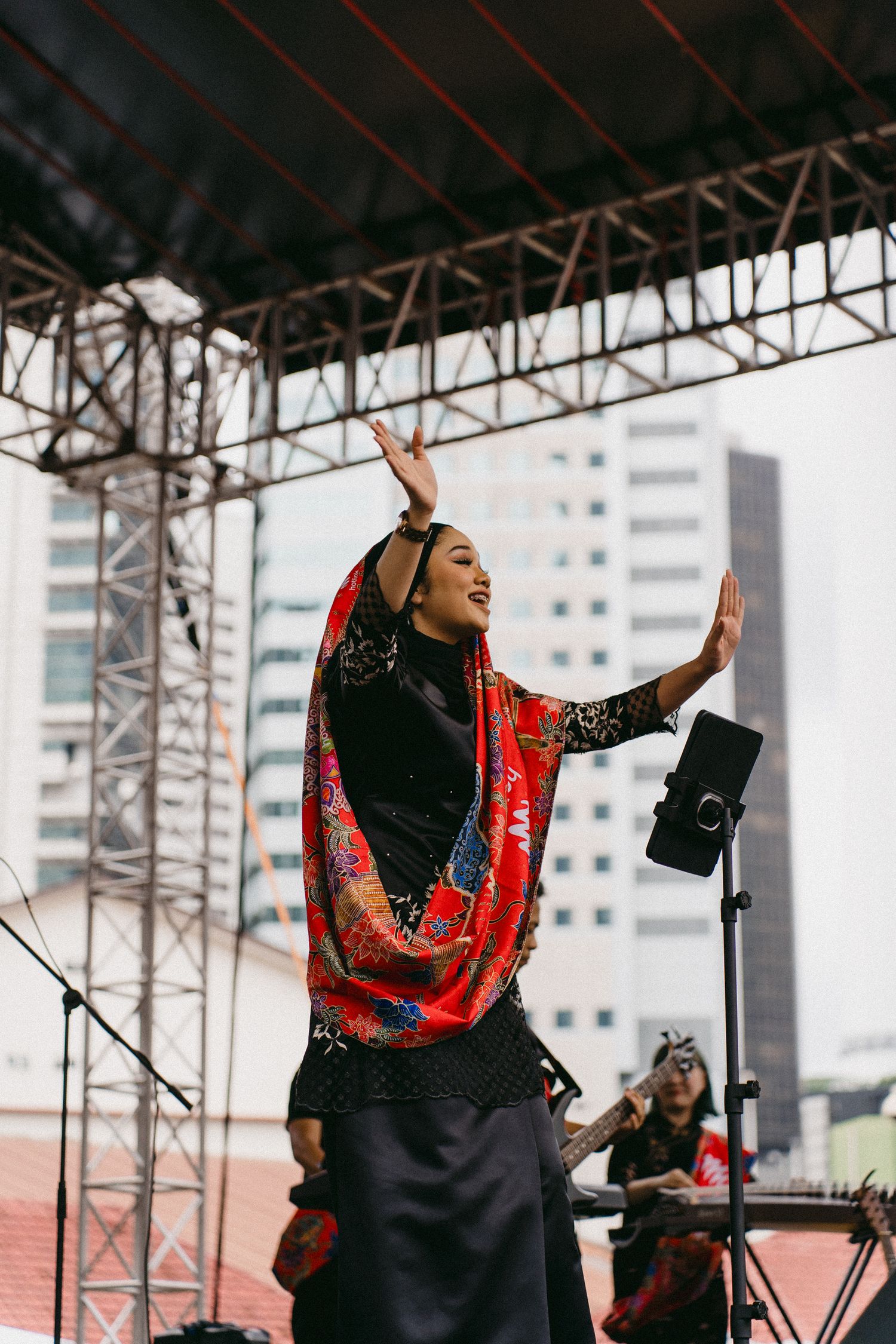Performer in black and red traditional dress singing passionately on outdoor stage.
