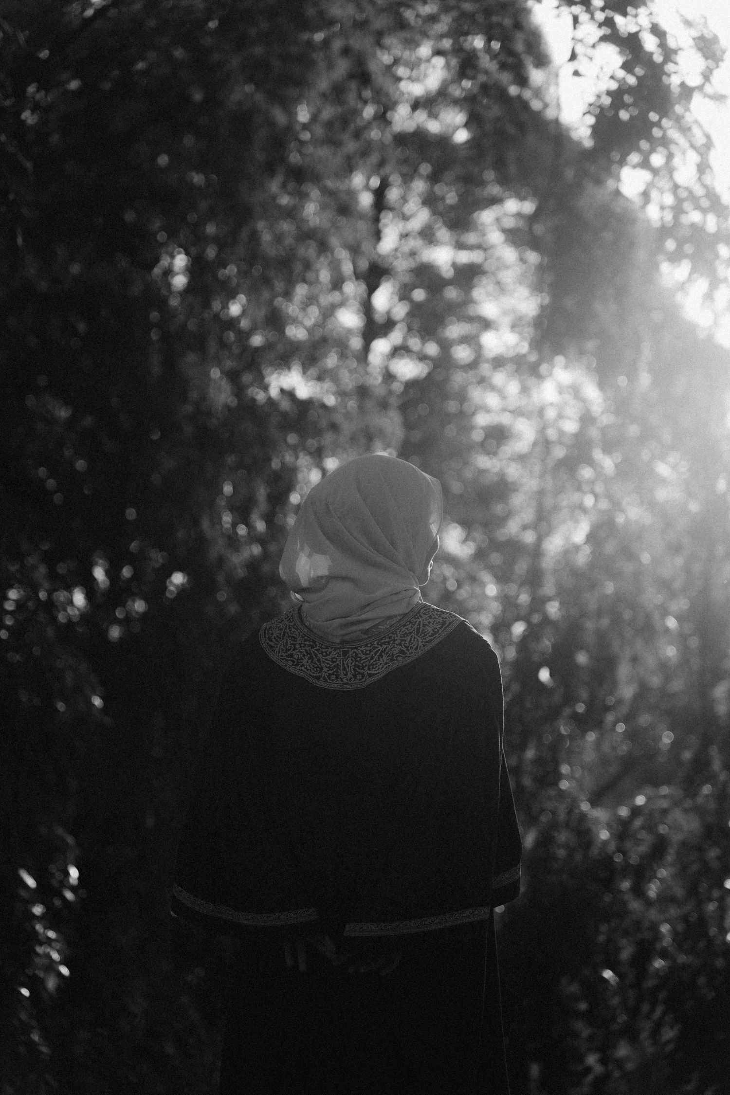 Silhouette of a person wearing a dark jacket against sunlit trees in a moody black and white composition.