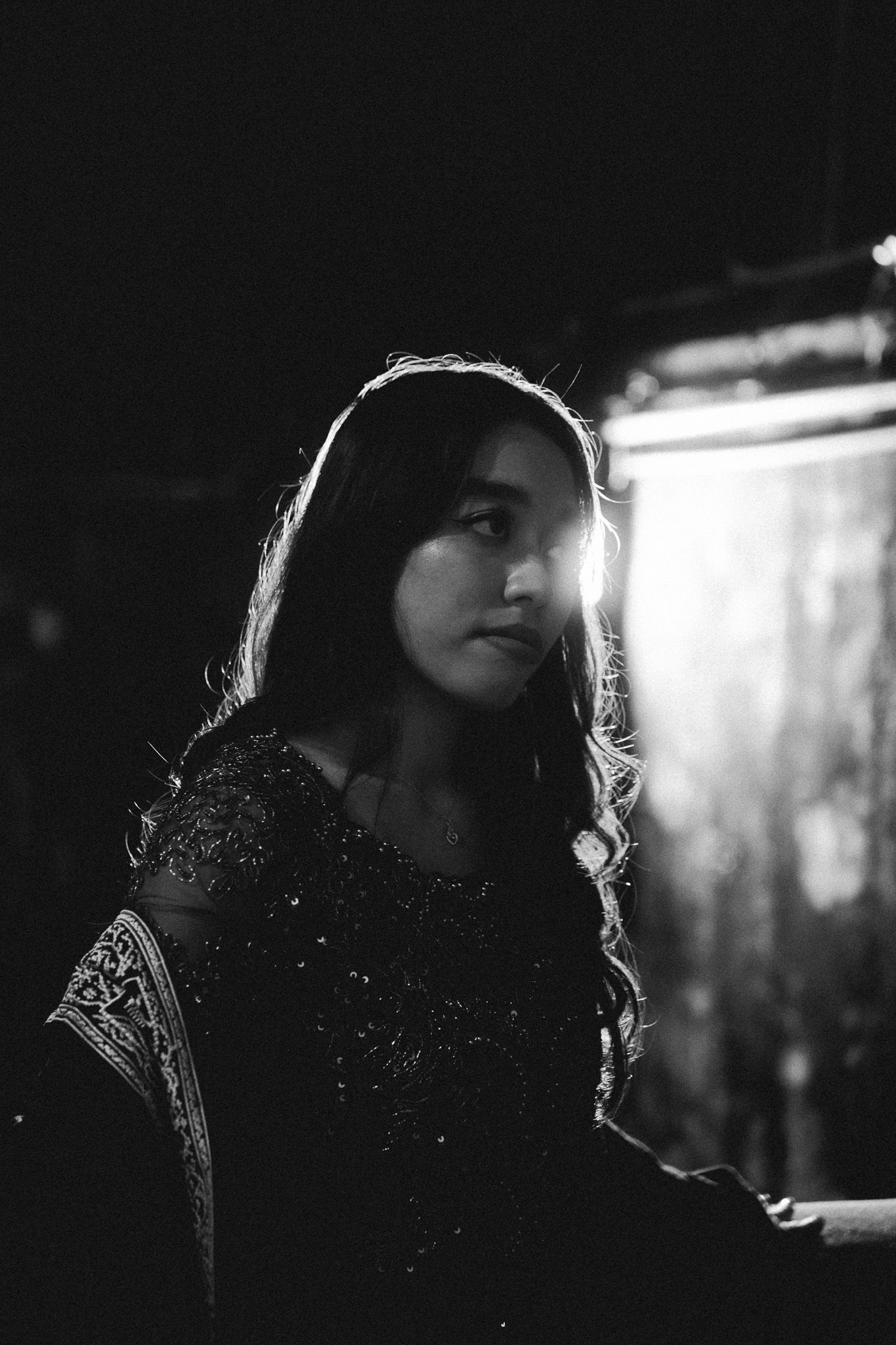 Dramatic black and white portrait of a young woman with long hair illuminated by a bright backlight.