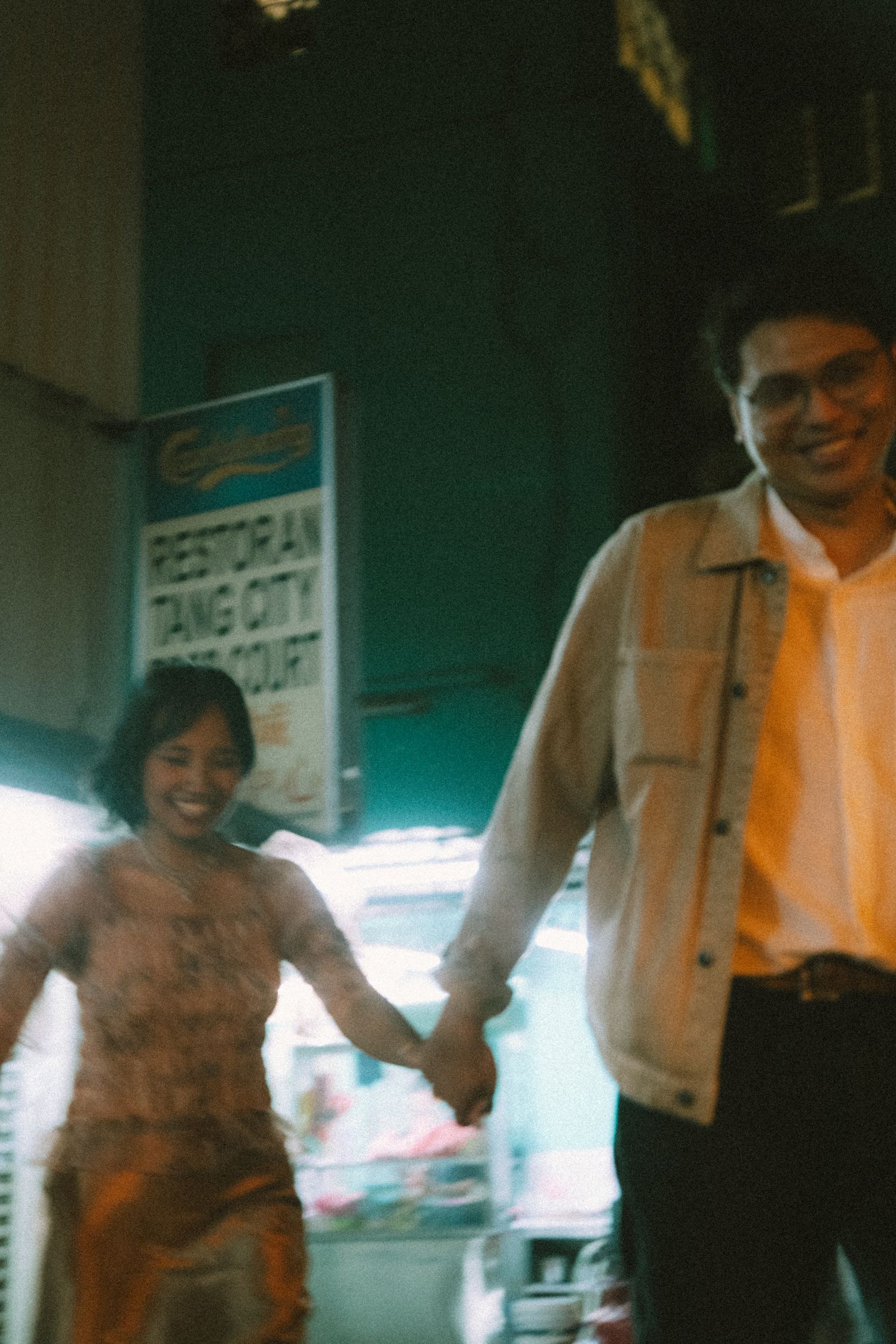 Couple smiling and holding hands outside Tang City food court under neon lights.