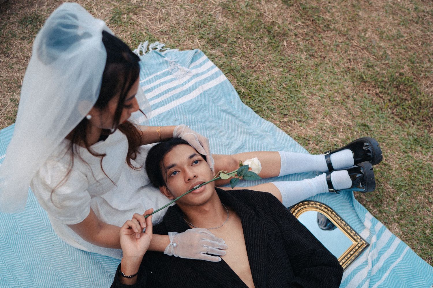 Wedding themed photoshoot with couple lying on blue blanket outdoors.