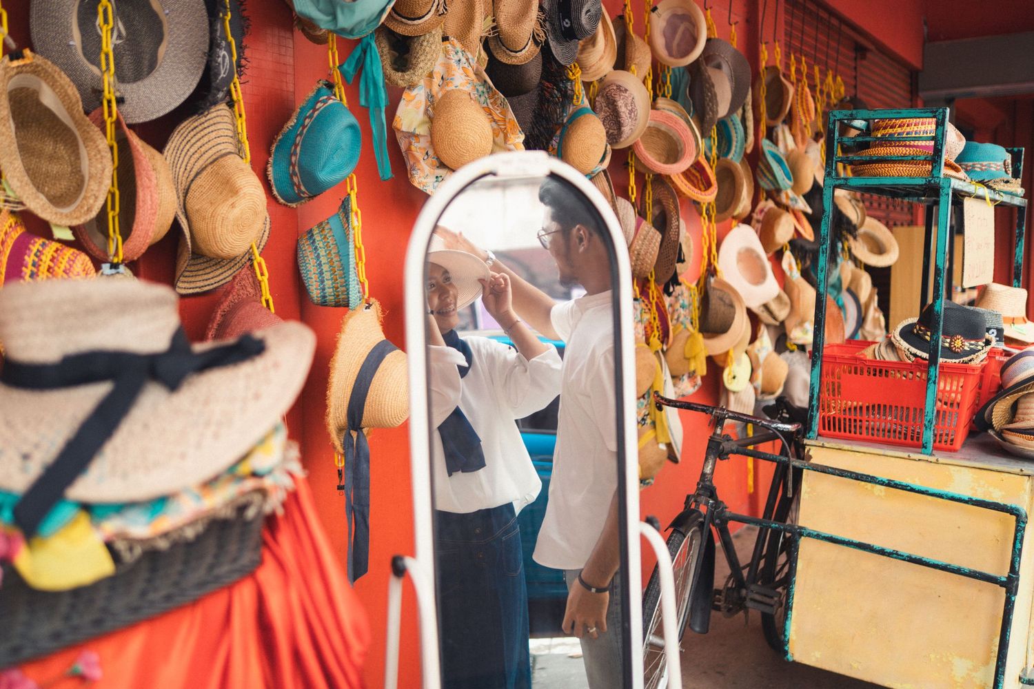 Person looks in mirror surrounded by hanging hats and accessories in a shop.
