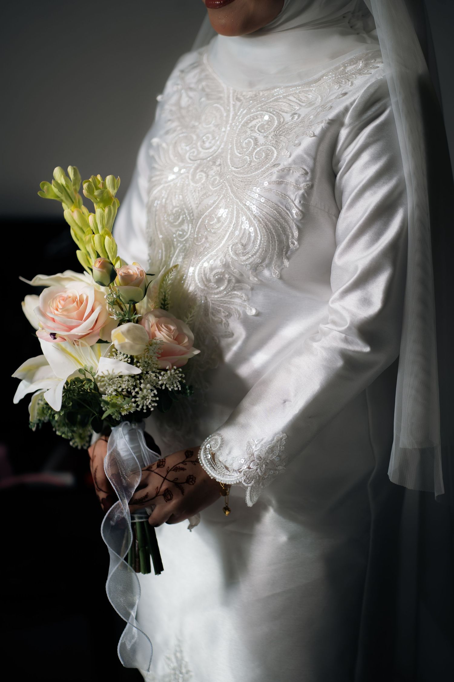 Close-up of elegant white wedding dress with embroidered bodice and bridal bouquet featuring roses and lilies.