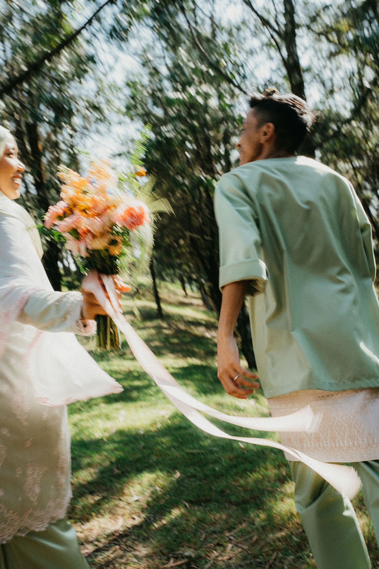 Couple in wedding attire dance joyfully in a sun-dappled garden setting, captured in artistic motion-blur sequence.