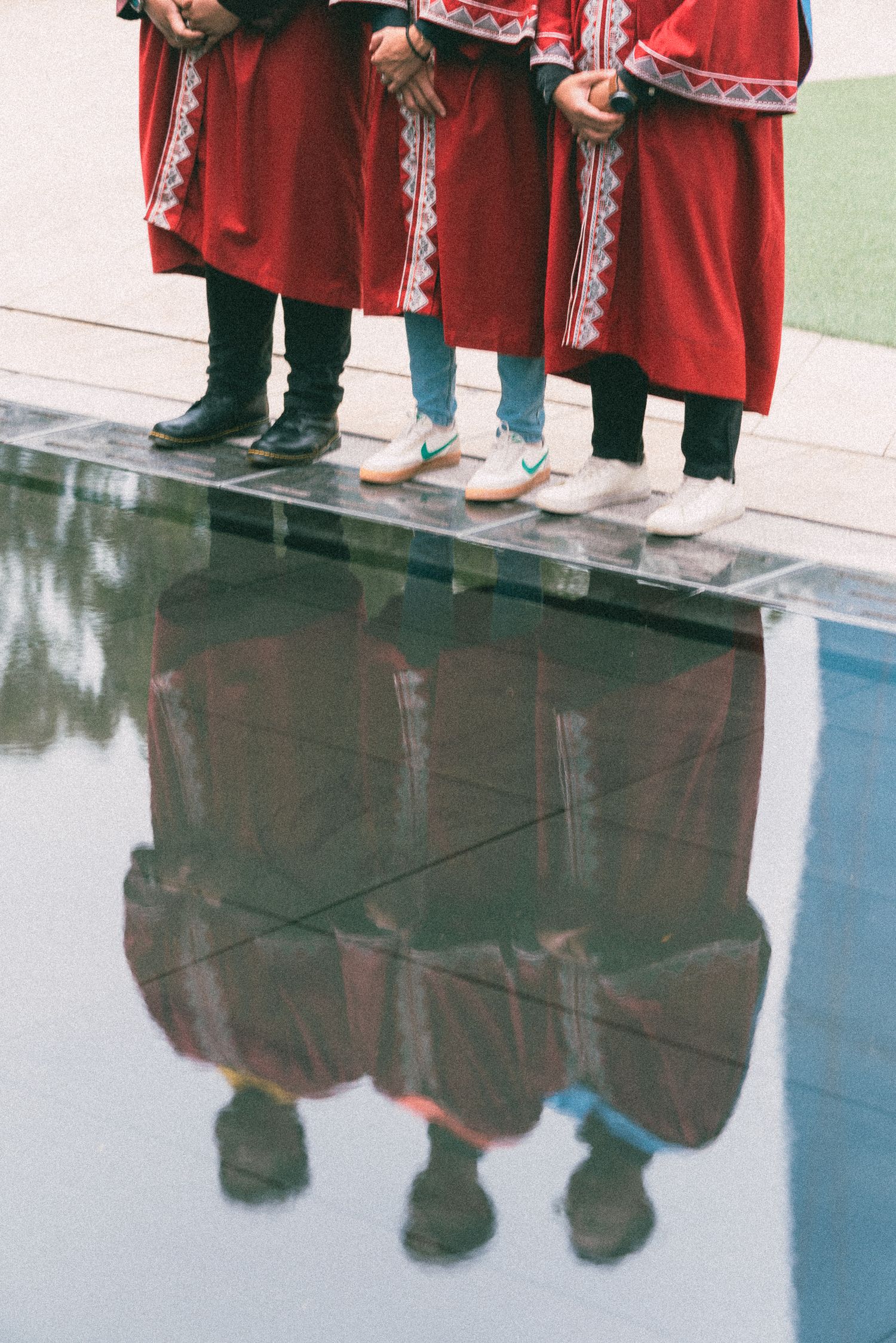 Three people in red traditional robes with their reflections in a puddle of water.