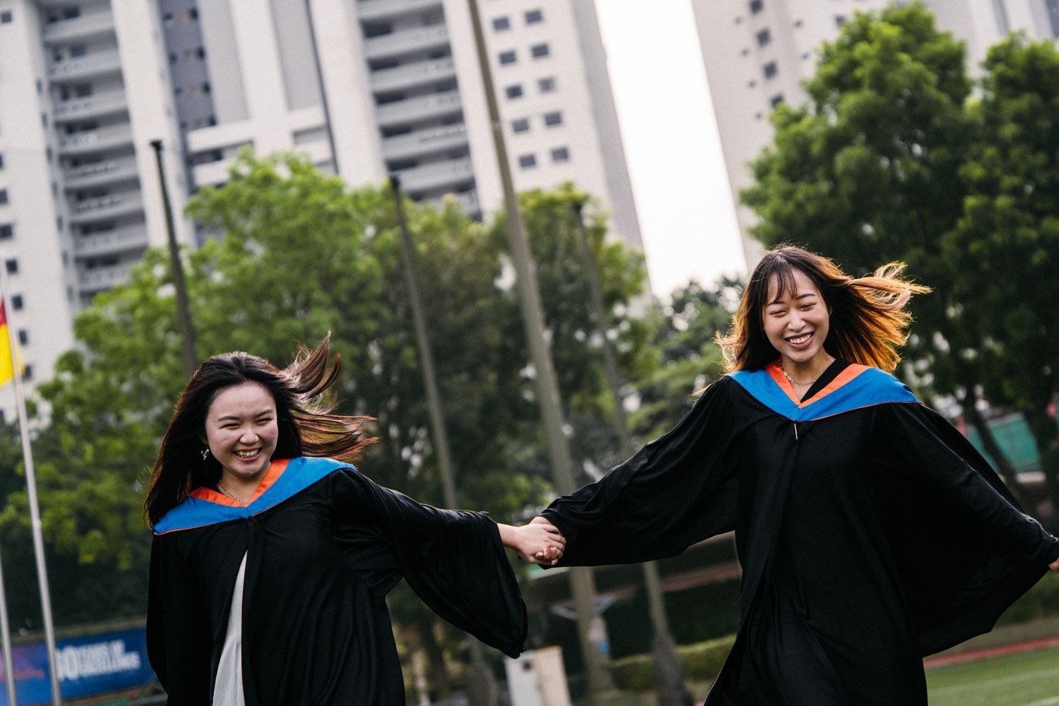 Joyful graduates in black and blue robes spinning and dancing outdoors on campus grounds.