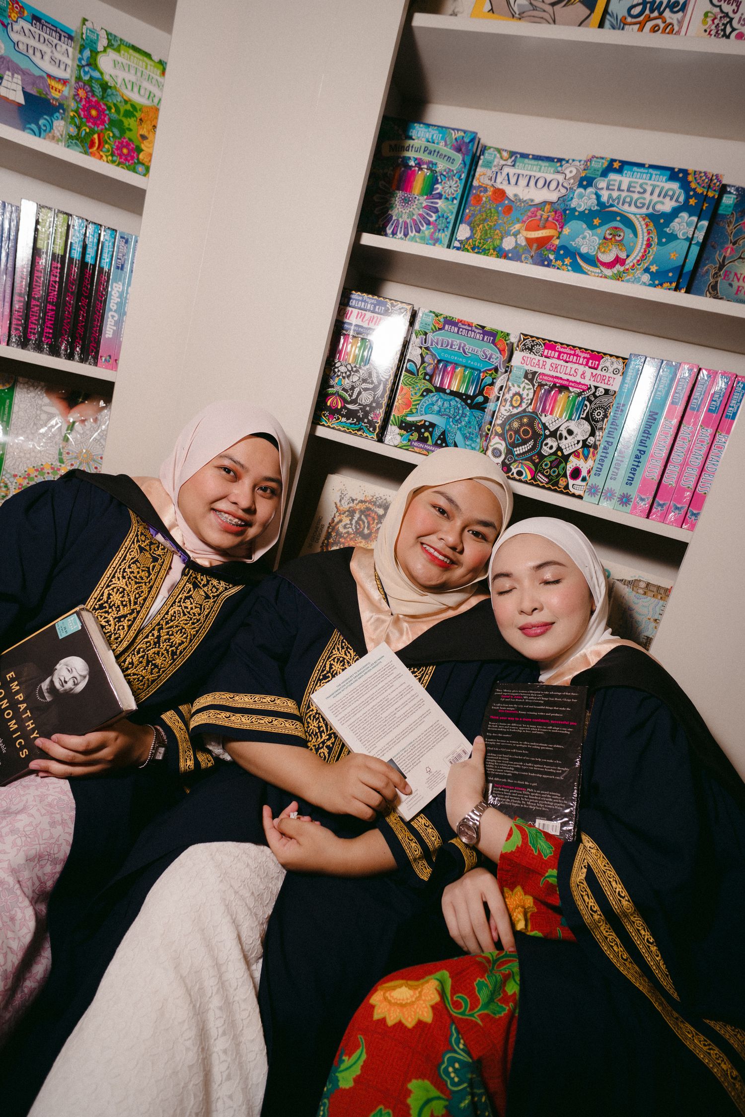 Students in graduation attire sharing joyful moment among bookshelves filled with colorful books.