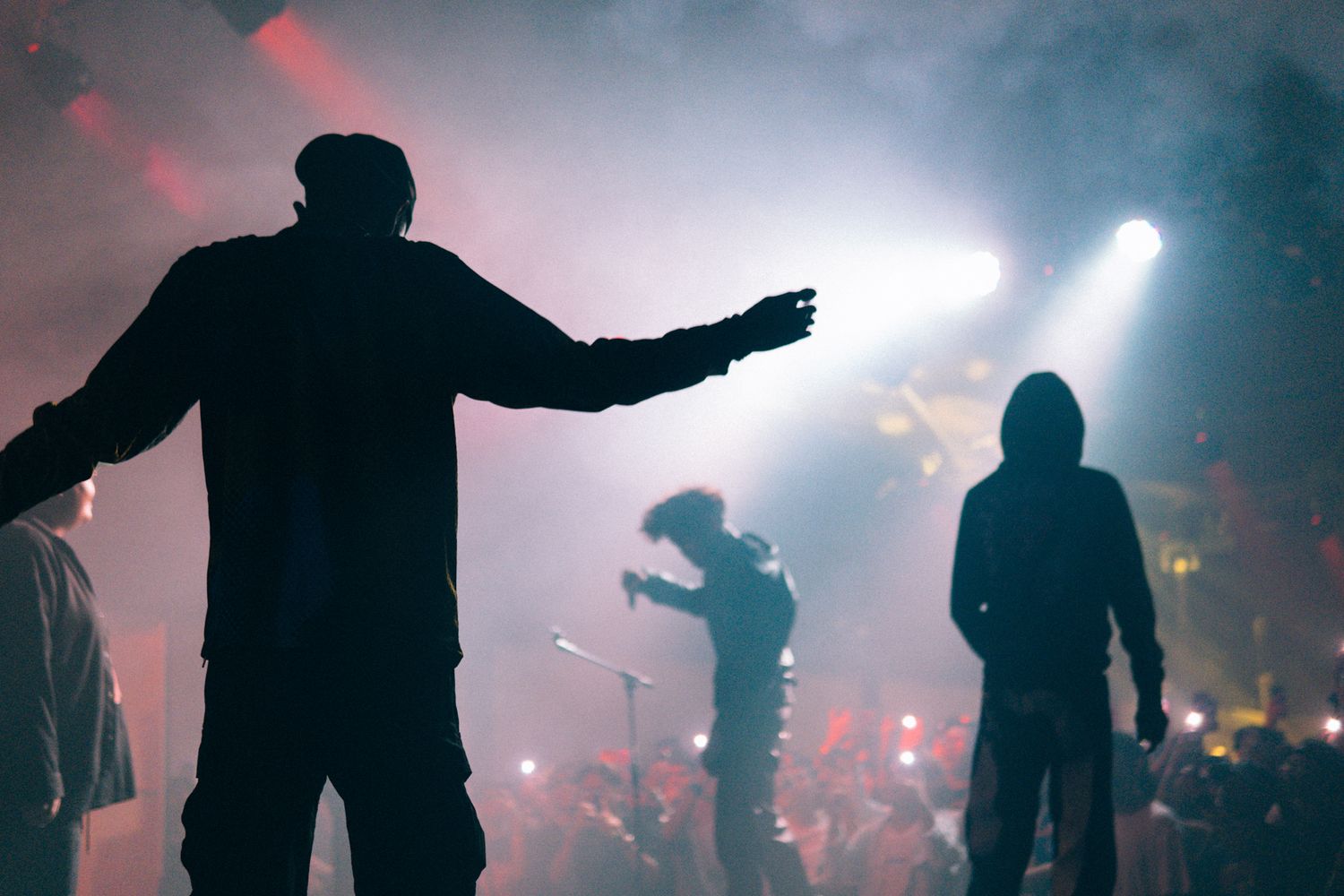 Silhouettes of performers on stage with dramatic red and white lighting effects during a concert.
