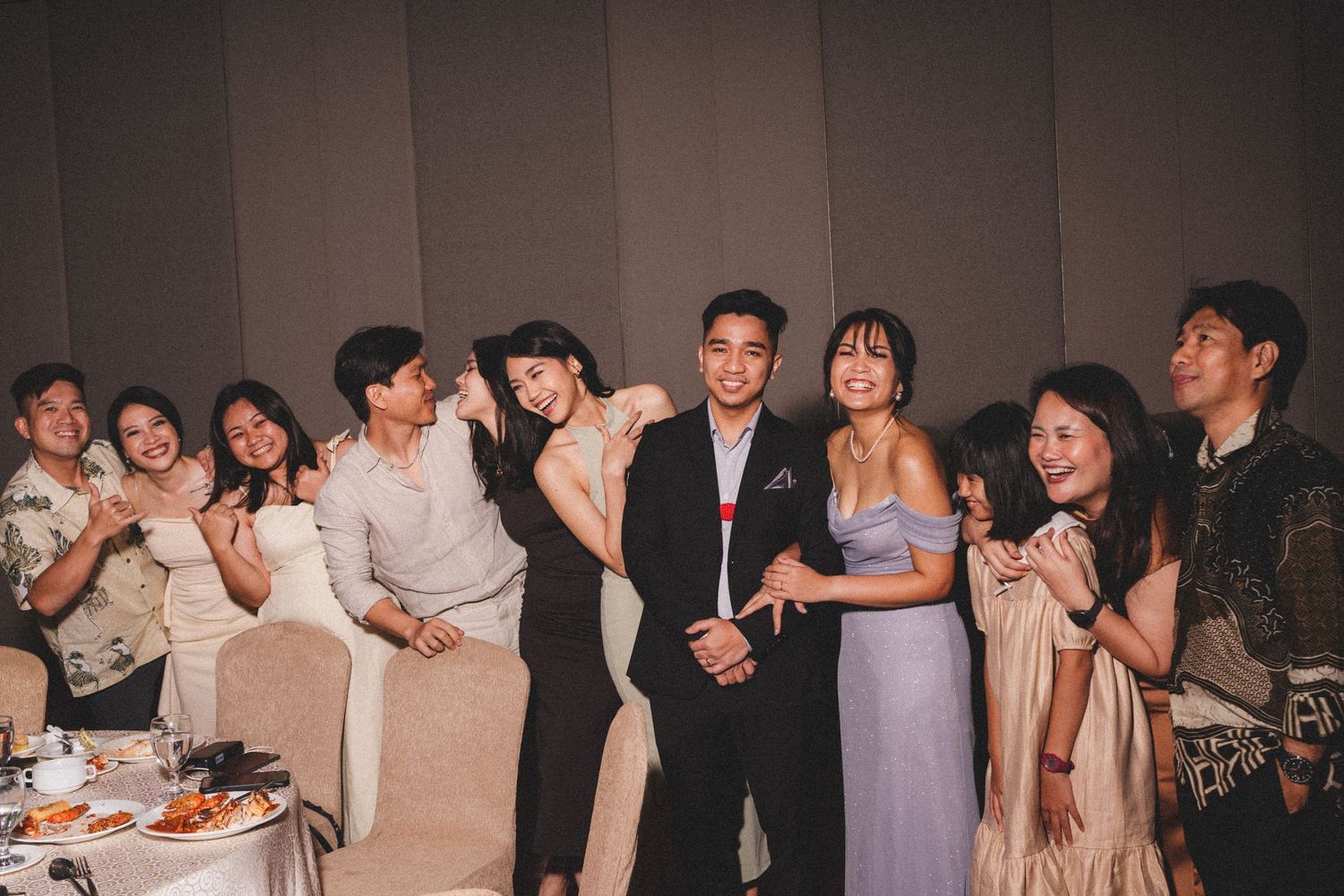 A group of party guests in formal attire laughing and having fun together at an indoor celebration.