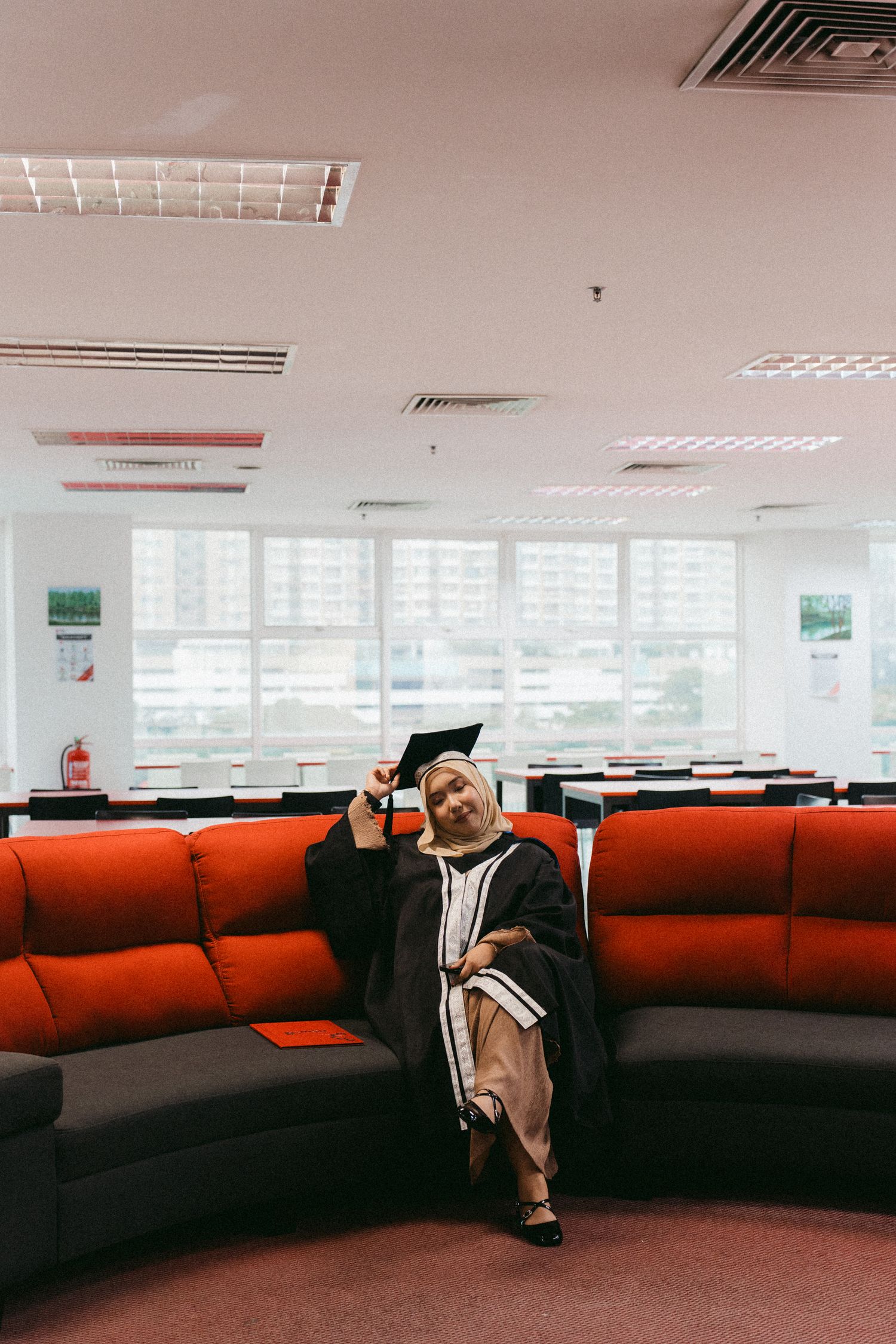 Someone relaxes on a curved red sofa in an office space with fluorescent lights and windows.