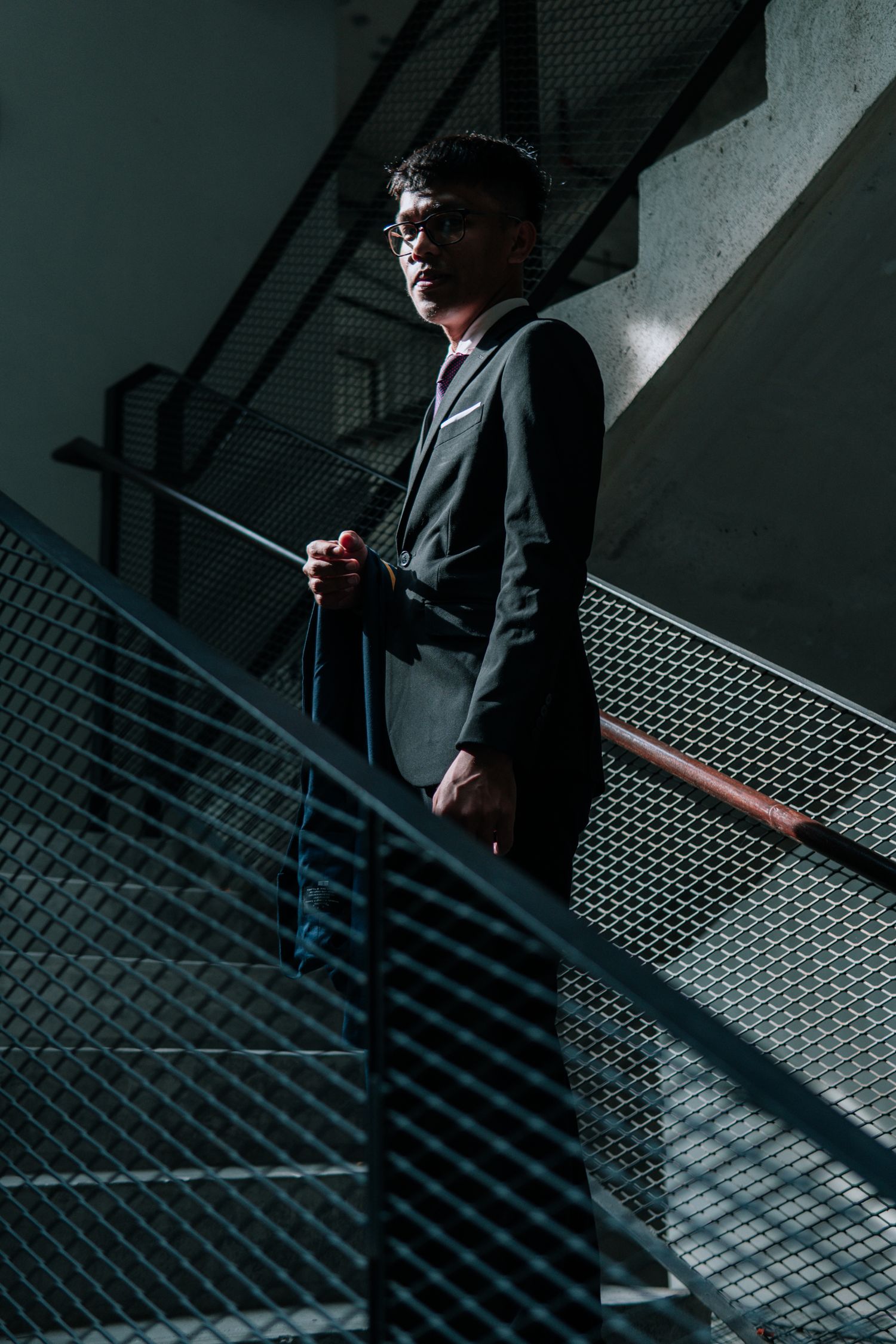 A silhouetted figure in a suit stands at a modern metal railing in moody lighting.