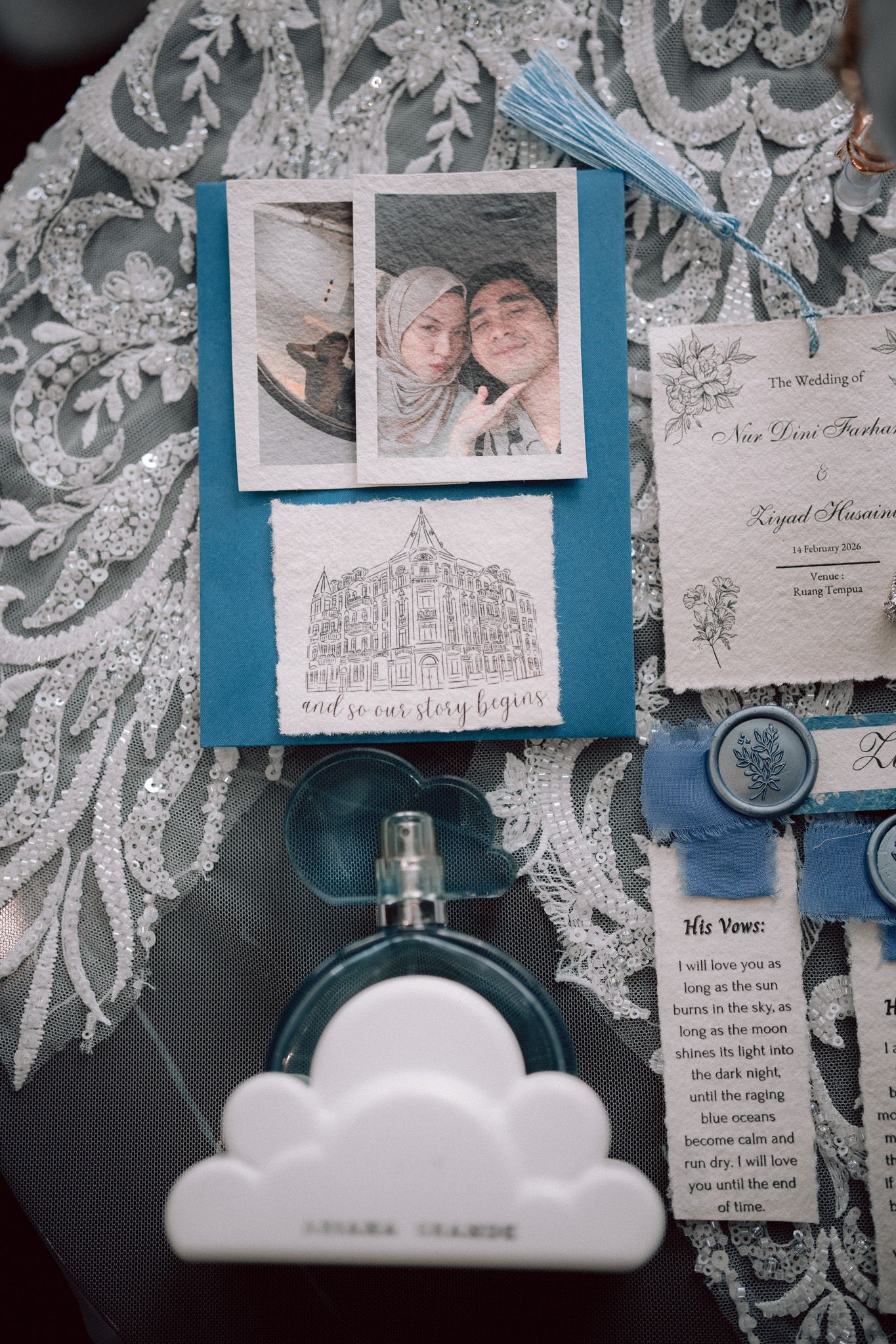 Wedding stationery flat lay featuring polaroid photo, blue invitation suite, vows card, and Ariana Grande perfume bottle.