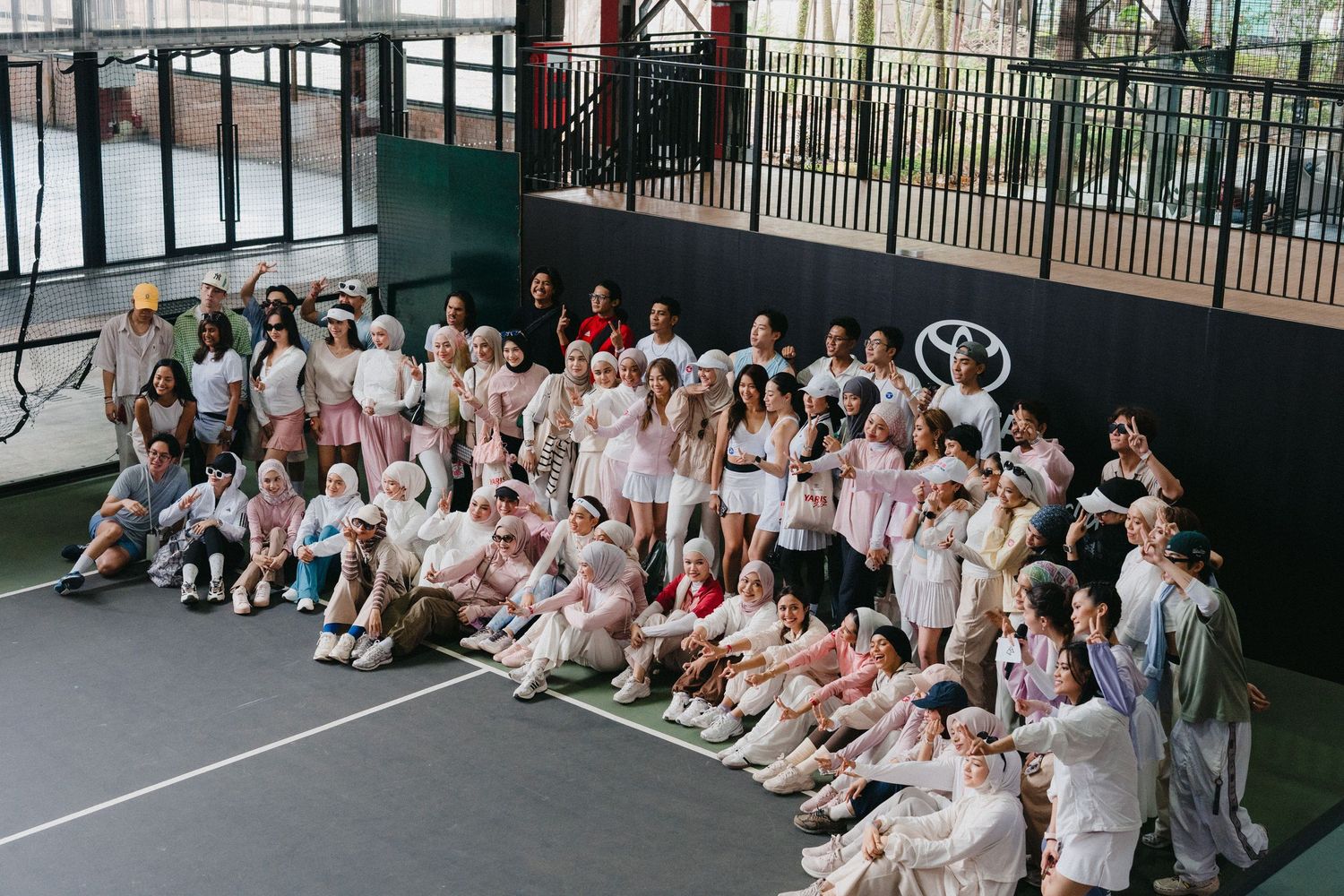 Large group in white dresses sitting together on outdoor tennis court steps for a formal group photo.
