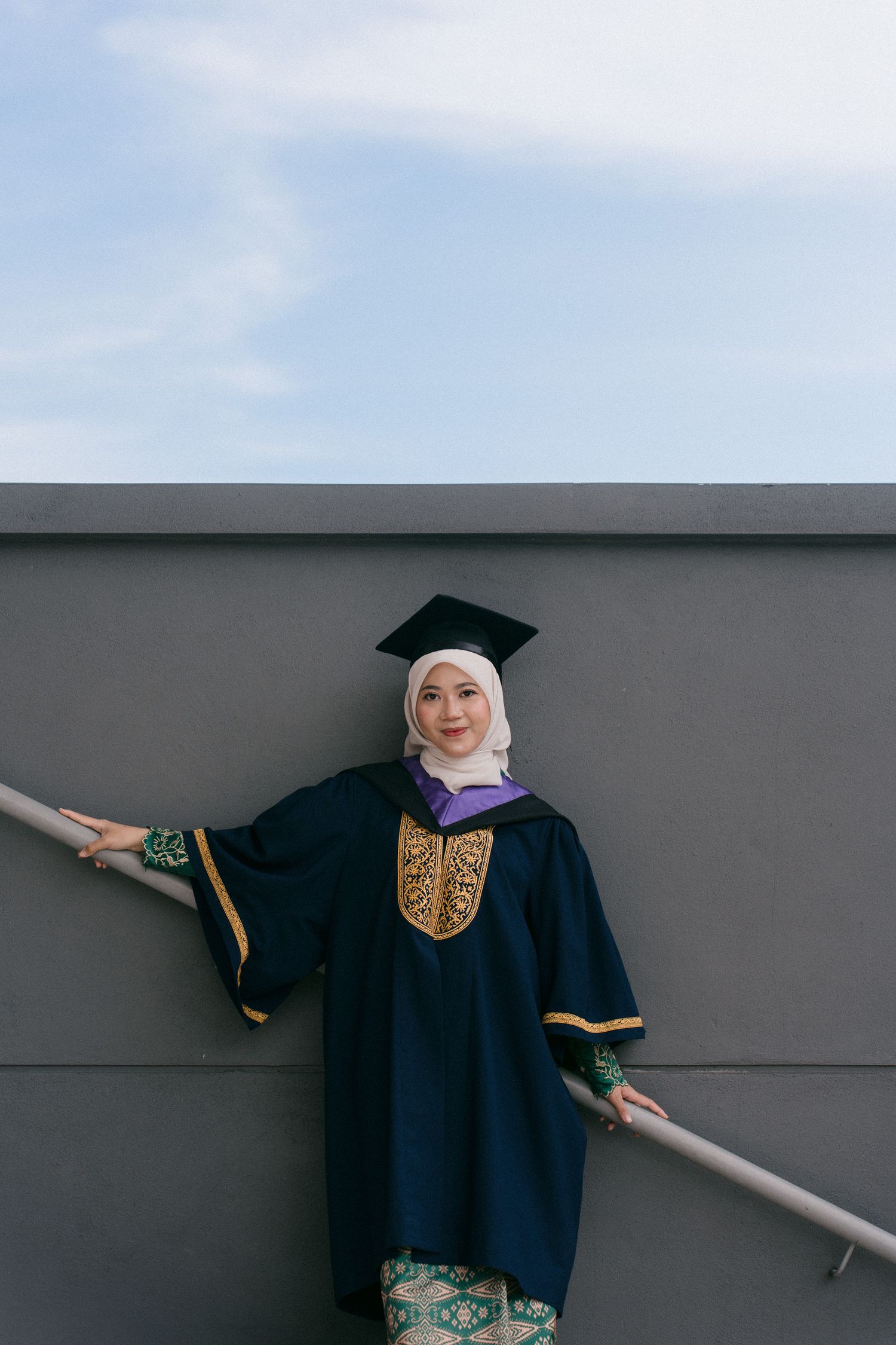 A graduate in black academic regalia poses against a gray wall in a series of artistic photos.