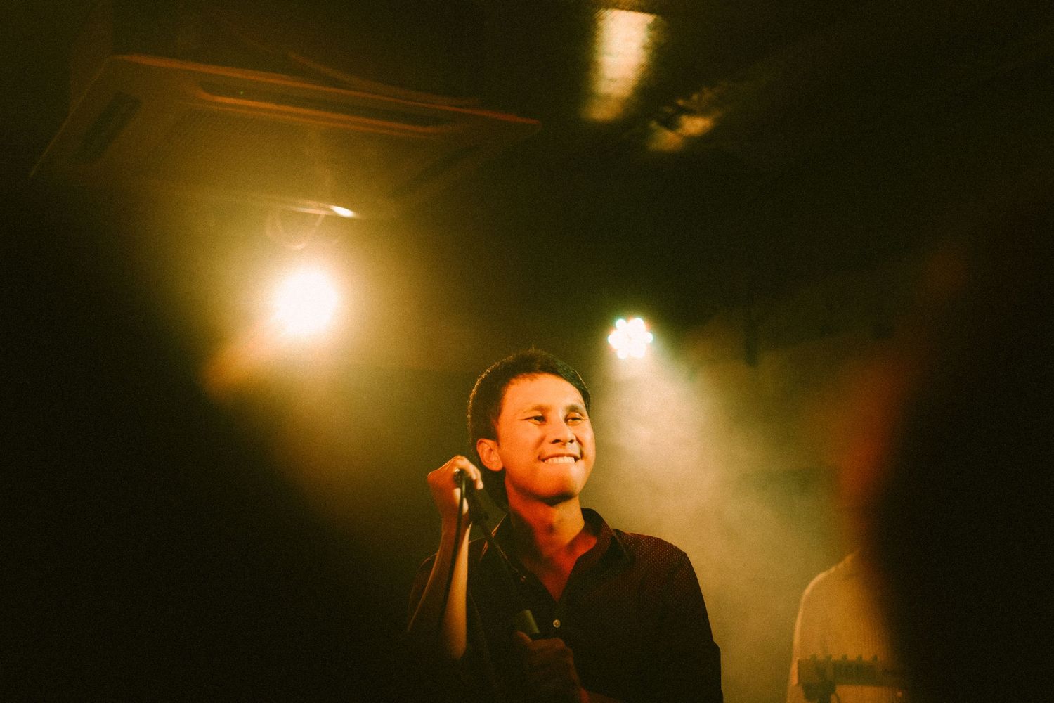A performer sings on stage under warm spotlights in a dark concert venue.