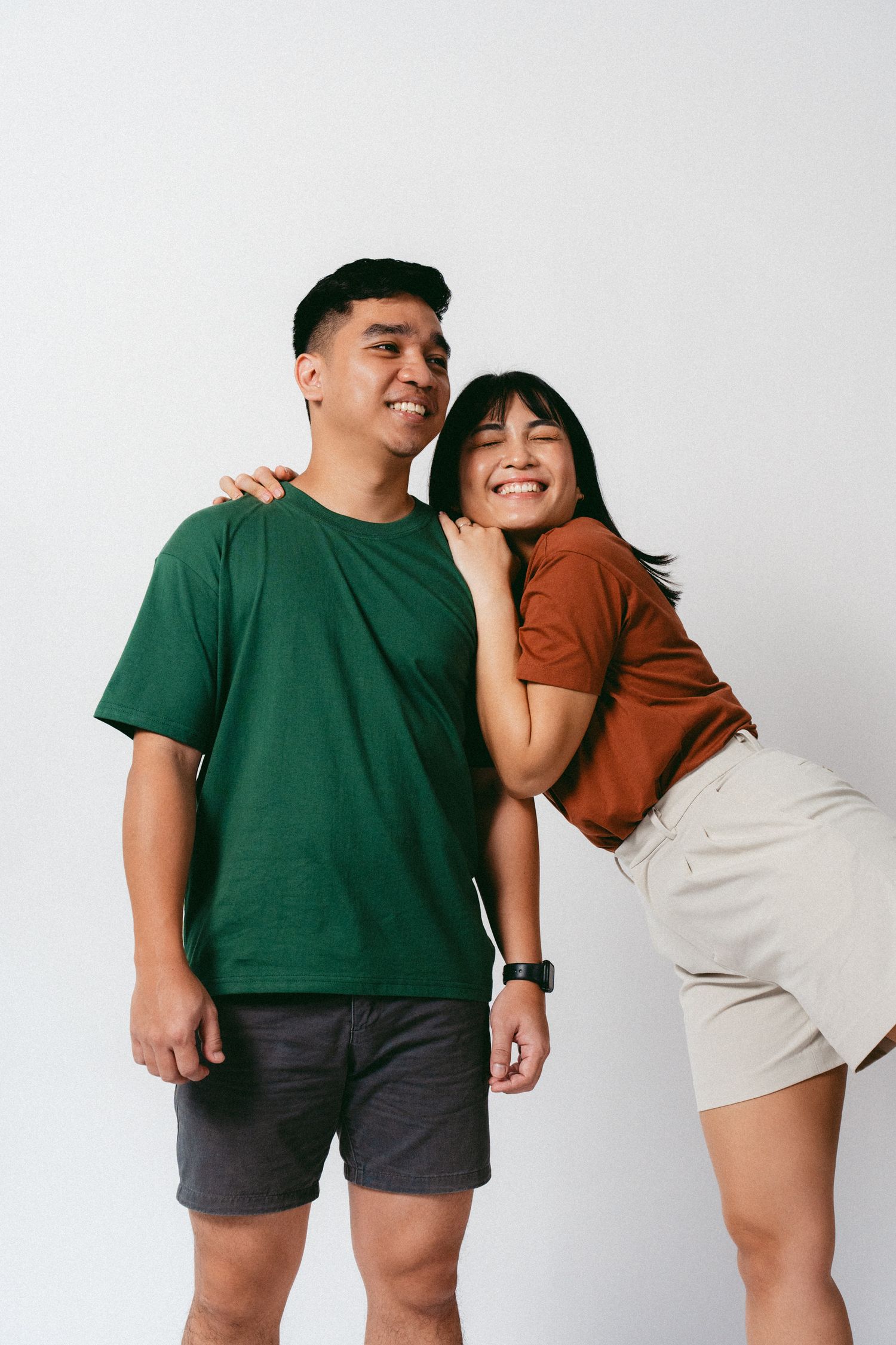 Playful couple in casual wear posing against white background with joyful expressions.