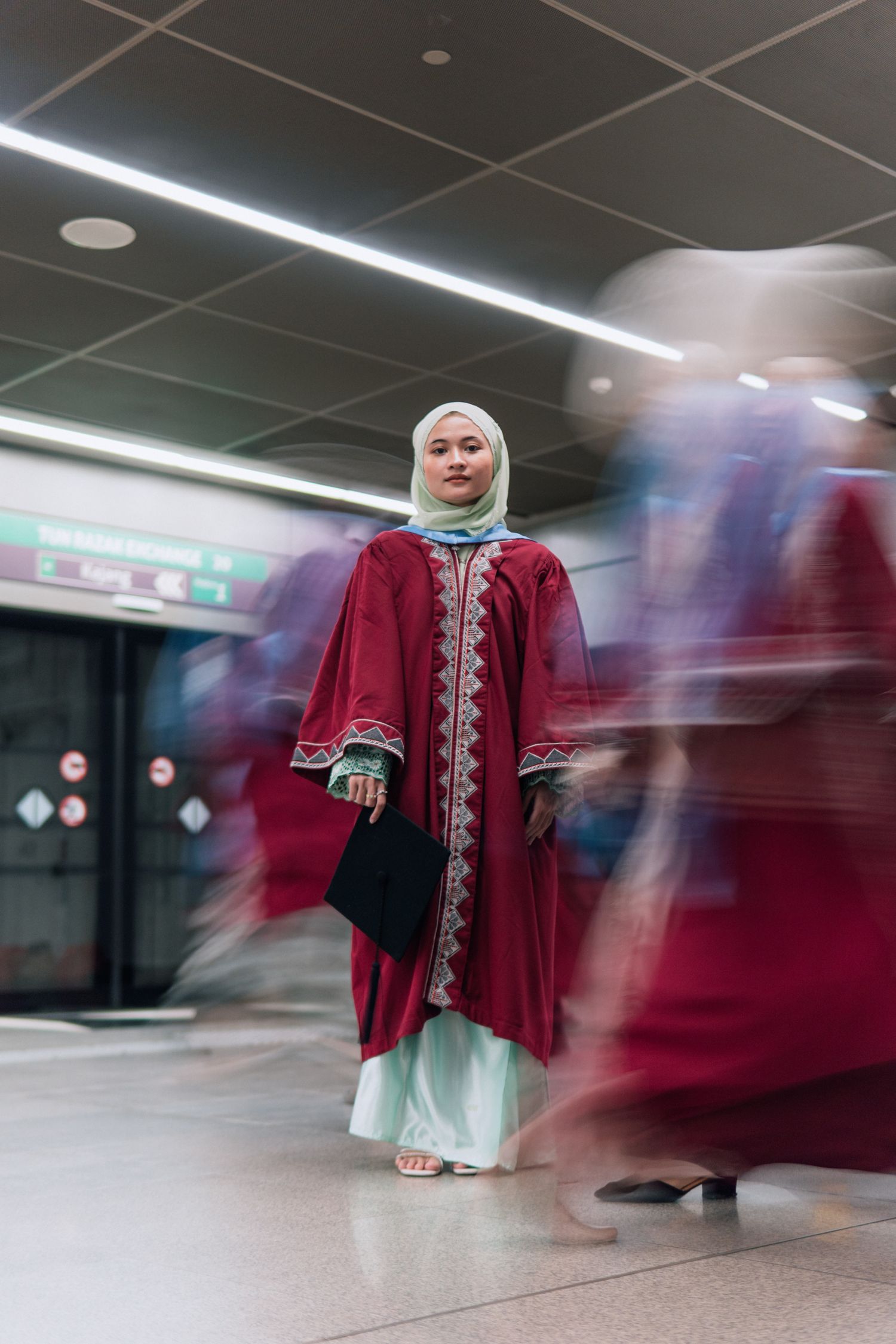 Figure in traditional red and white attire stands still while others move in motion blur around them.