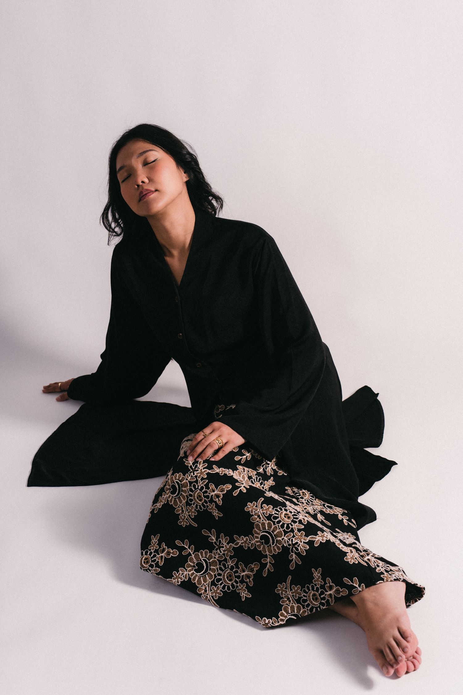 Flowing black dress with intricate embroidered details photographed against a white studio backdrop.